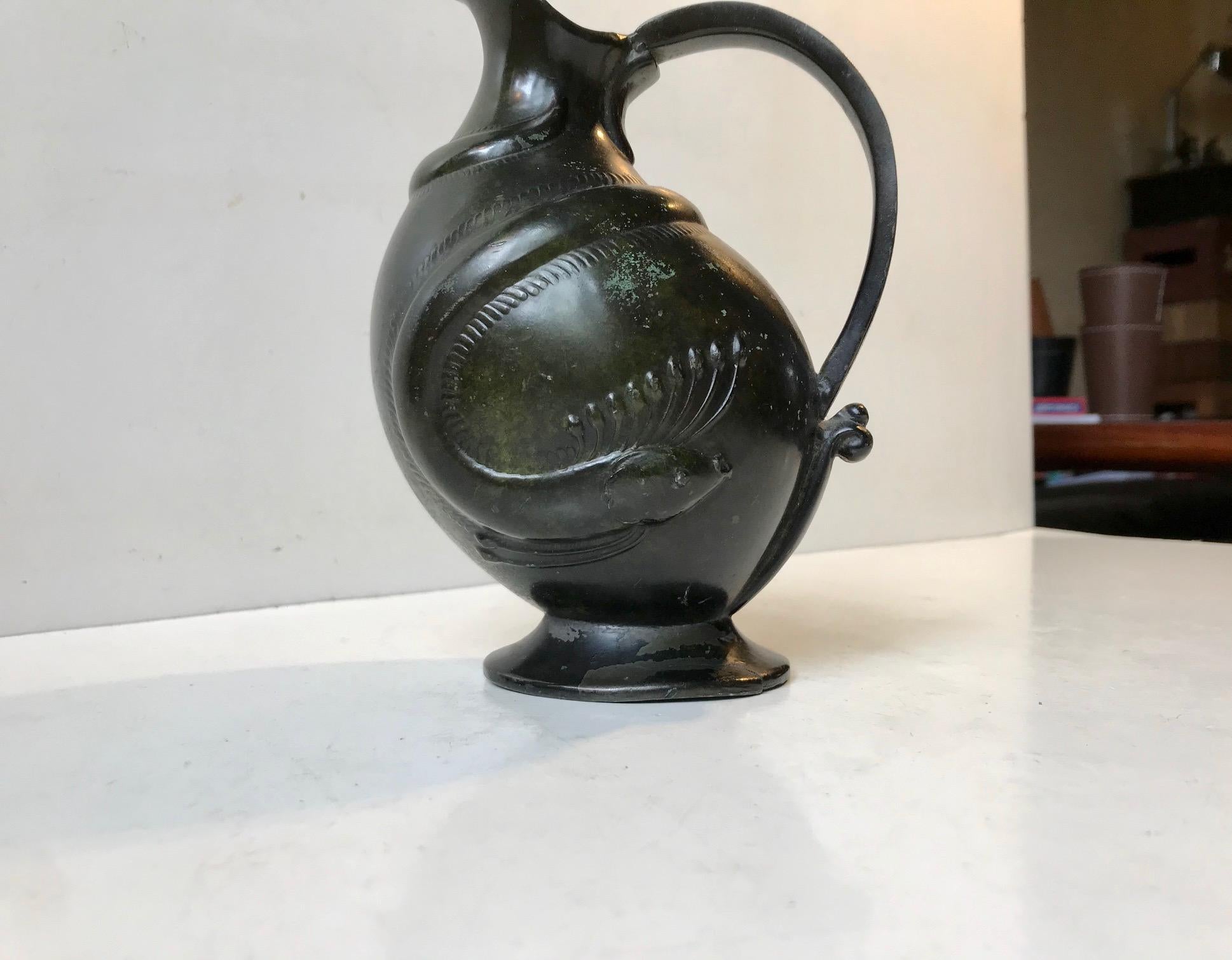 A very early Art Deco styled jug made in Denmark during the 1920s. Japanese or Chinese inspired decor. It is made from Disko Metal an alloy made mainly from pewter with applied verdigris patina in order to mimic bronze. It has a relief motif of a