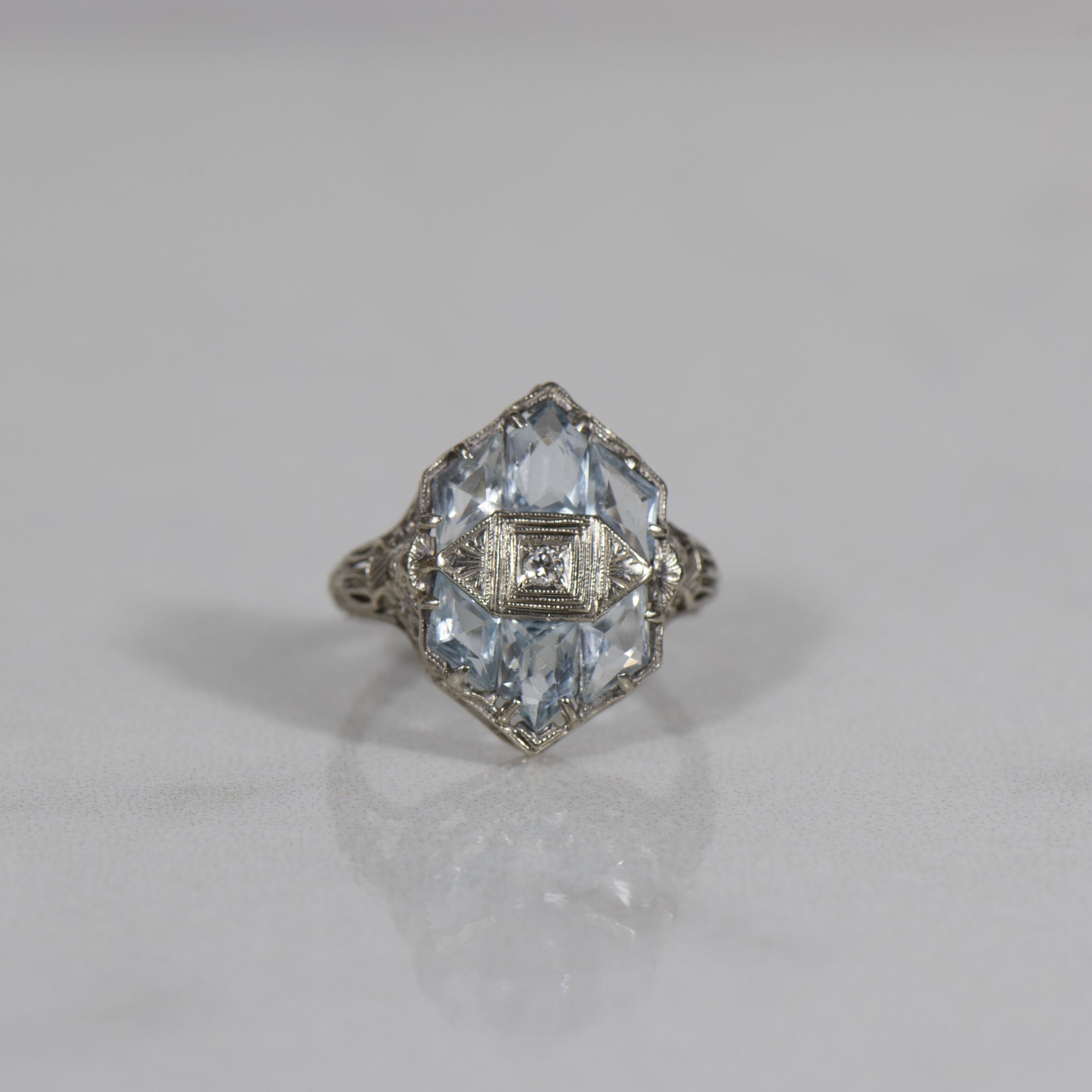 Dieser von der Art déco inspirierte Ring aus luxuriösem 14-karätigem Weißgold ist ein faszinierendes Beispiel für geometrische Eleganz. Im Mittelpunkt des Rings steht ein bezaubernder sechseckiger Aqua-Edelstein, der sorgfältig aus Aquamarinen im