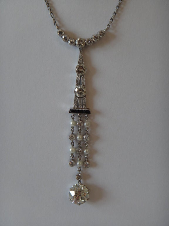 1920's. Art déco serti d'un diamant central pesant 2,40 ct, pureté : VS1, couleur : cape. 38 diamants pesant 1,54 ct., onyx et perles. Monté en platine. Chaîne en or blanc 14K. Poids total 8,84 g. 
Longueur : 2.56 in ( 6,5 cm ) Longueur avec chaîne