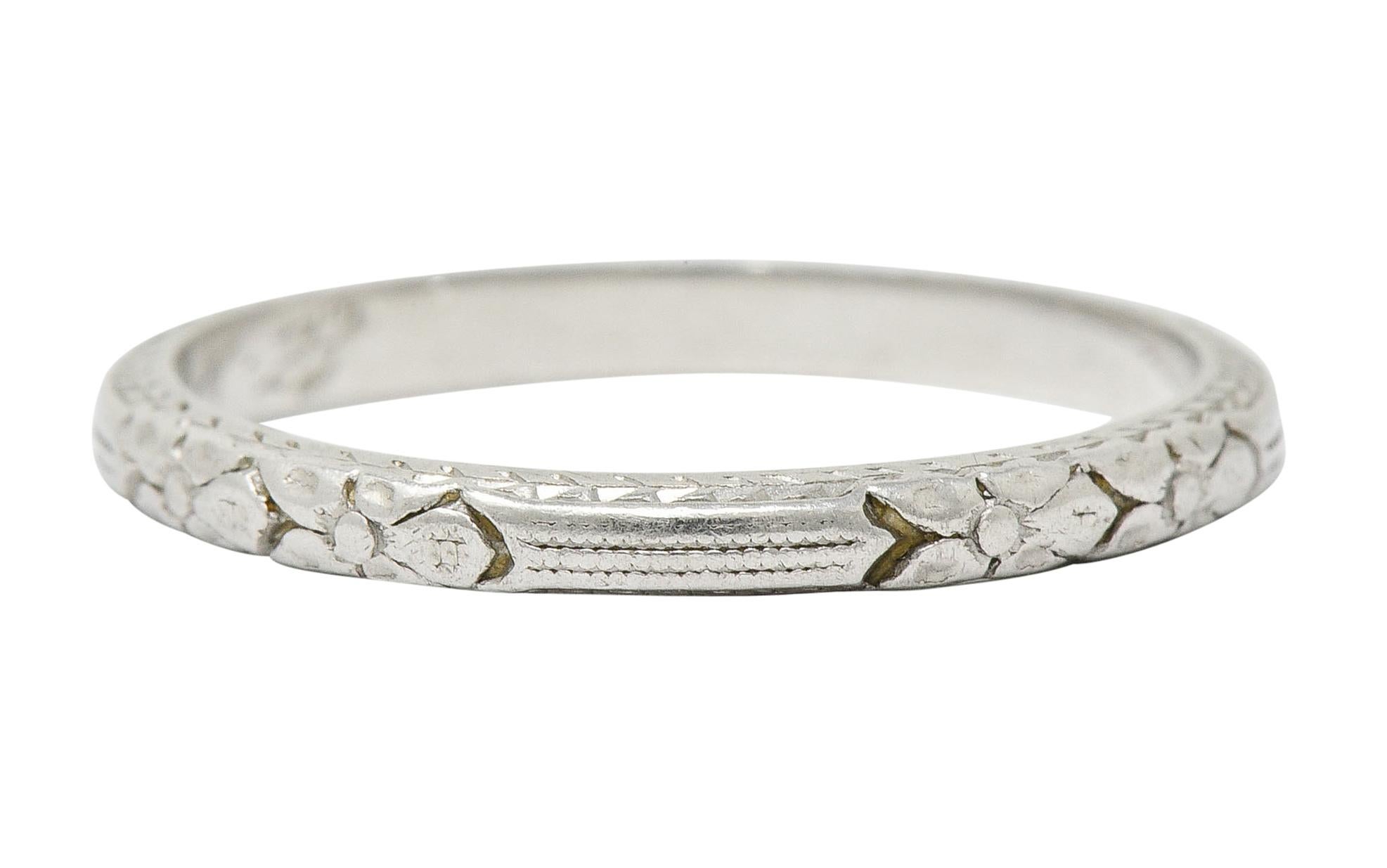 Band ring designed with parallel lines accented by double flower stations

With profile edges depicting a deeply engraved wheat motif

Stamped Platinum

With dated inscription circa 1920s

Ring Size: 5 1/4 & not sizable

Measures: 1.9 mm wide and