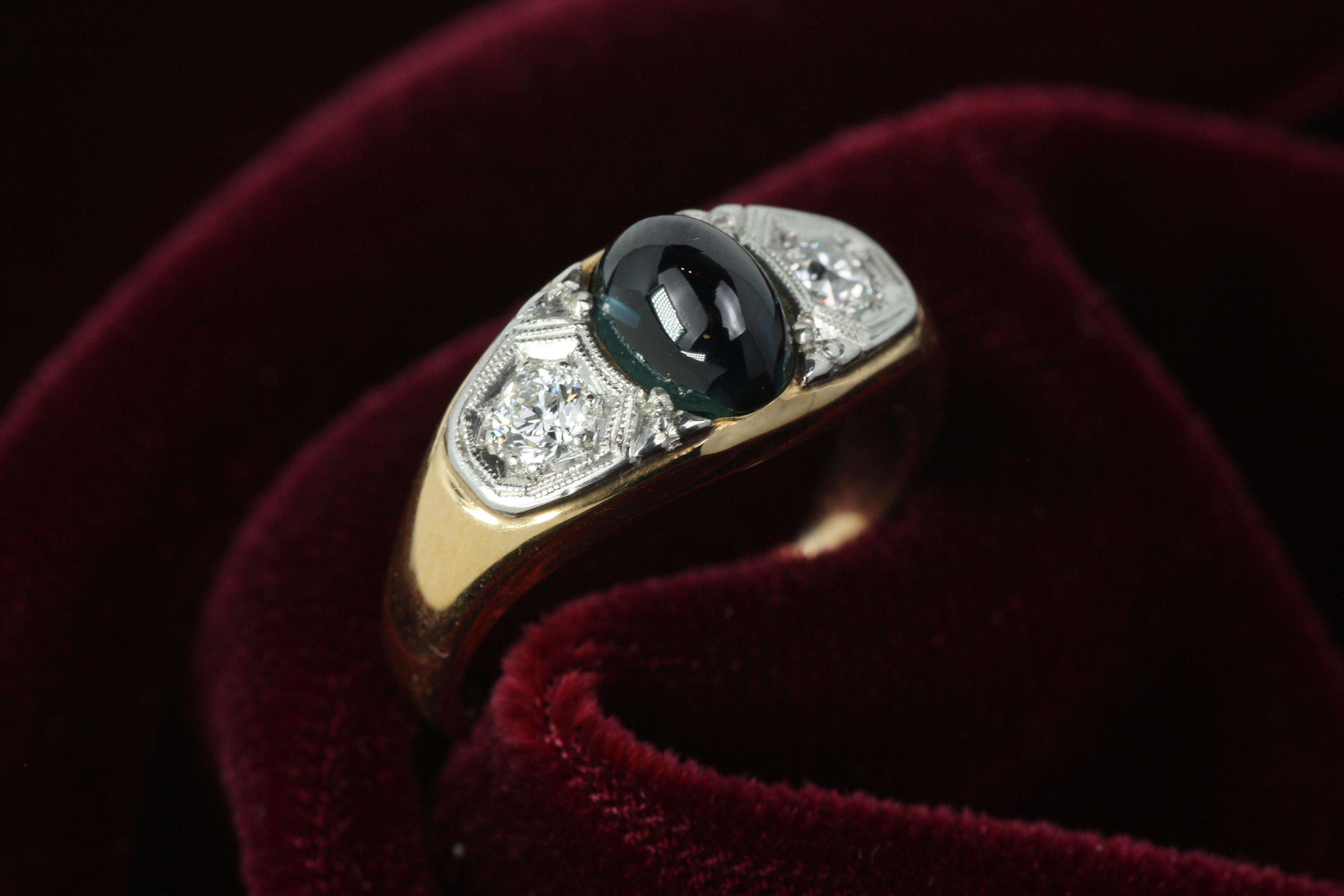 Une bague unisexe de la fin de l'Art déco, vers 1920, de notre collection de bijoux anciens de Bracken Jewelers. Il comprend un saphir bleu verdâtre naturel taillé en cabochon pesant environ 1,30 carat et deux diamants de taille ancienne totalisant