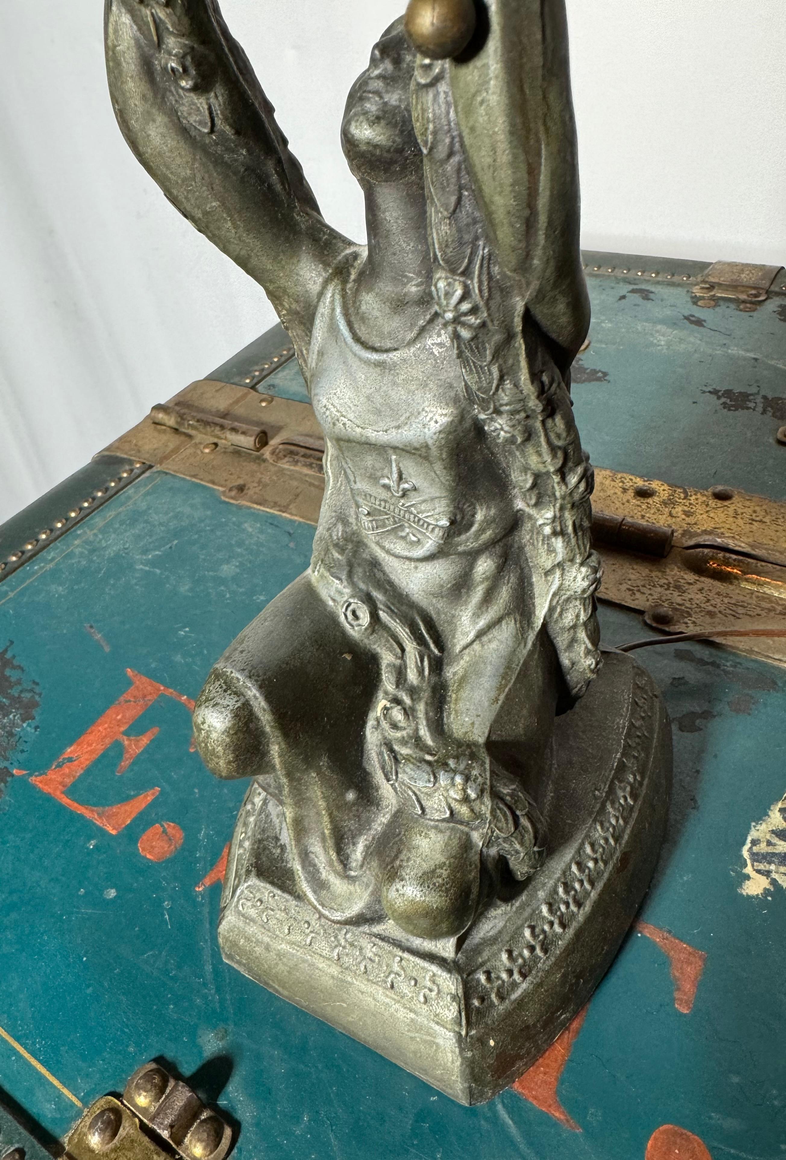 Lampada da tavolo in metallo spelta Art Deco raffigurante Giovanna d'Arco della La Belle Specialty Company, 1920 circa. La base è composta da Giovanna d'Arco inginocchiata e vestita che regge un paralume in vetro opalino bianco flash a forma di