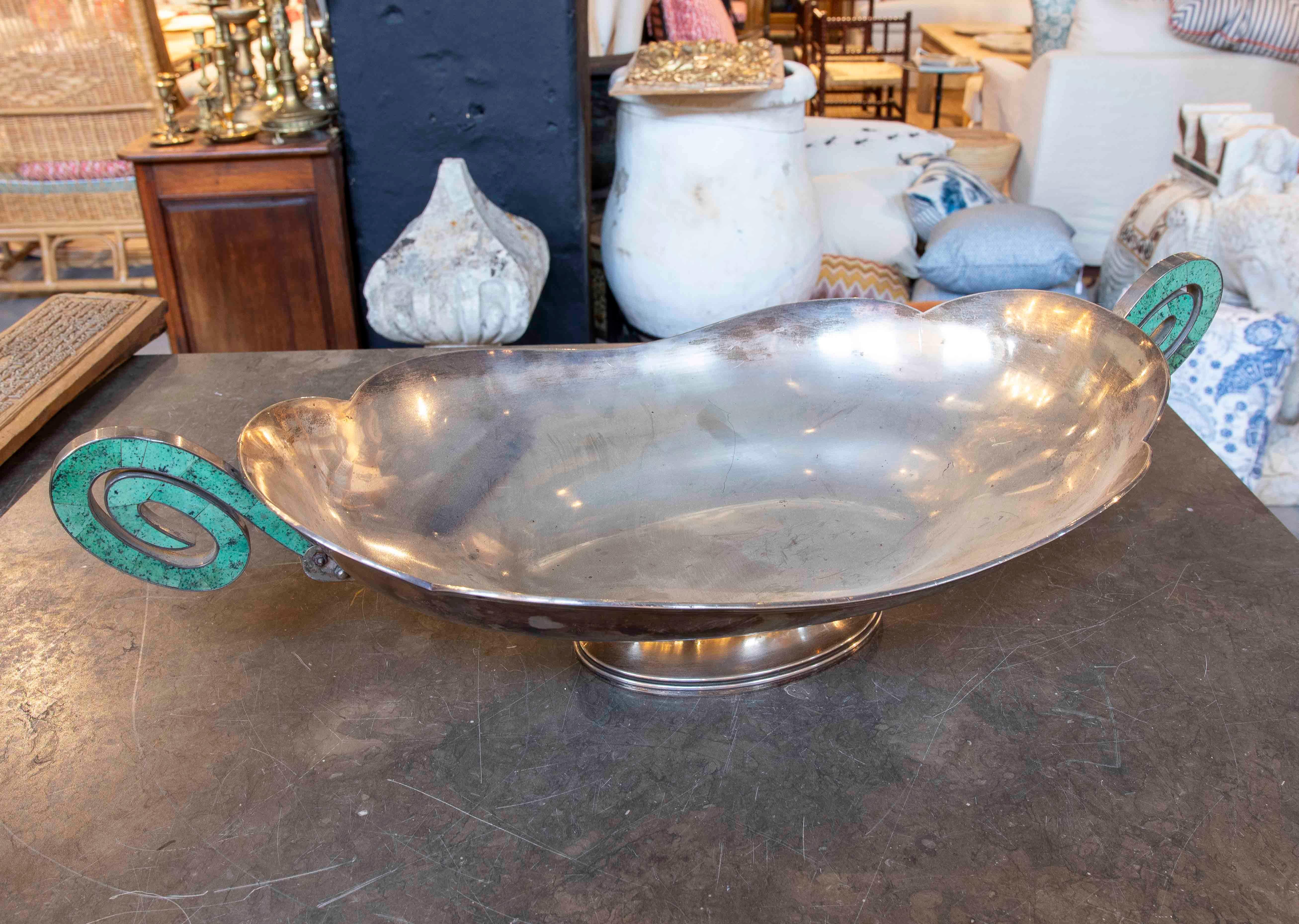Elegant centerpiece in silver with a classic design in the **Art Deco** style, characteristic of the 1920s and 1930s. The piece features an oval body with curved edges and side handles in a spiral shape adorned with turquoise inlays, a distinctive