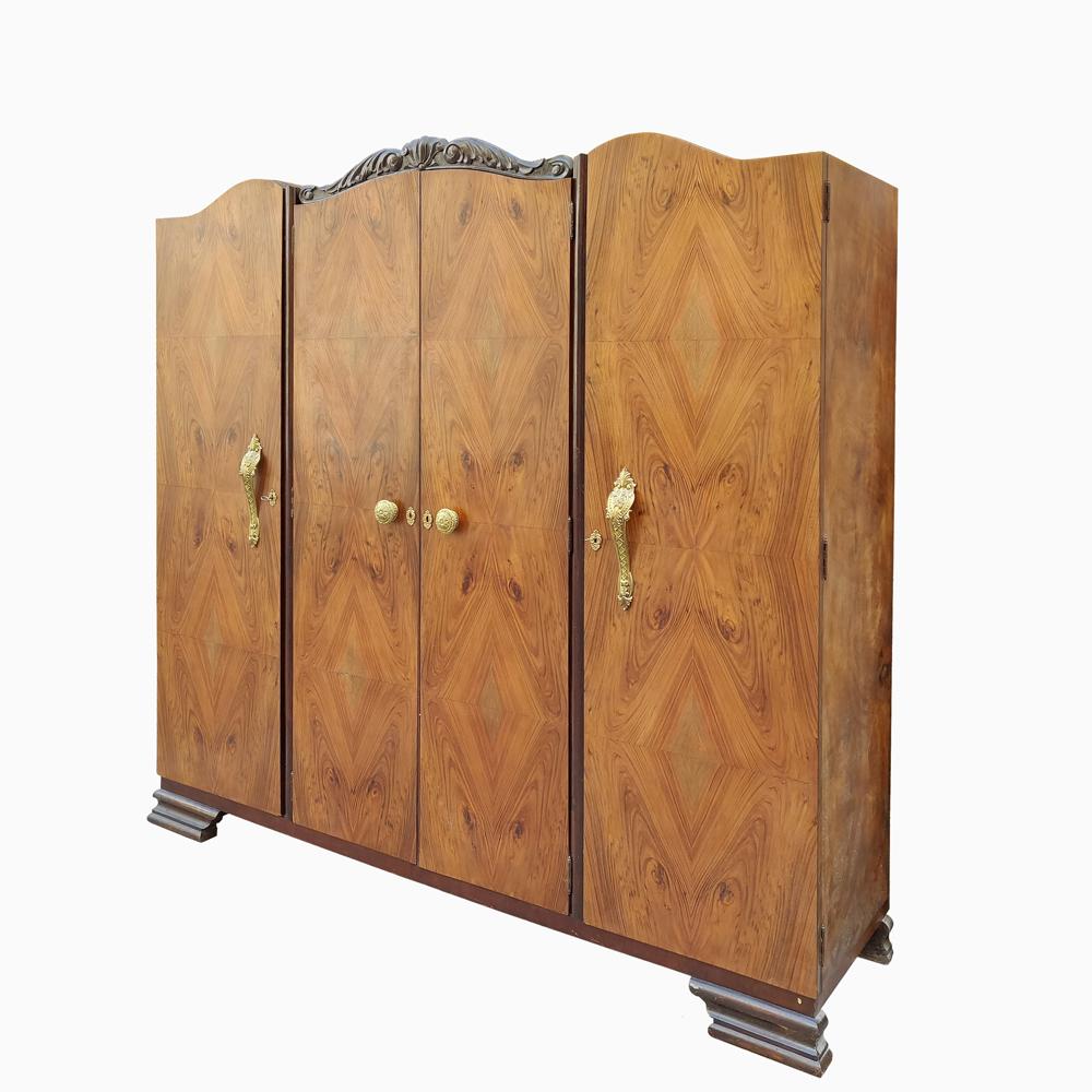 An Art Deco 4-door wardrobe finished in walnut veneer. The walnut wood has a beautiful diamond wood grain pattern mixing many shades of golden brown. The two outer doors have large golden handles with French vintage style detailing. The two inner