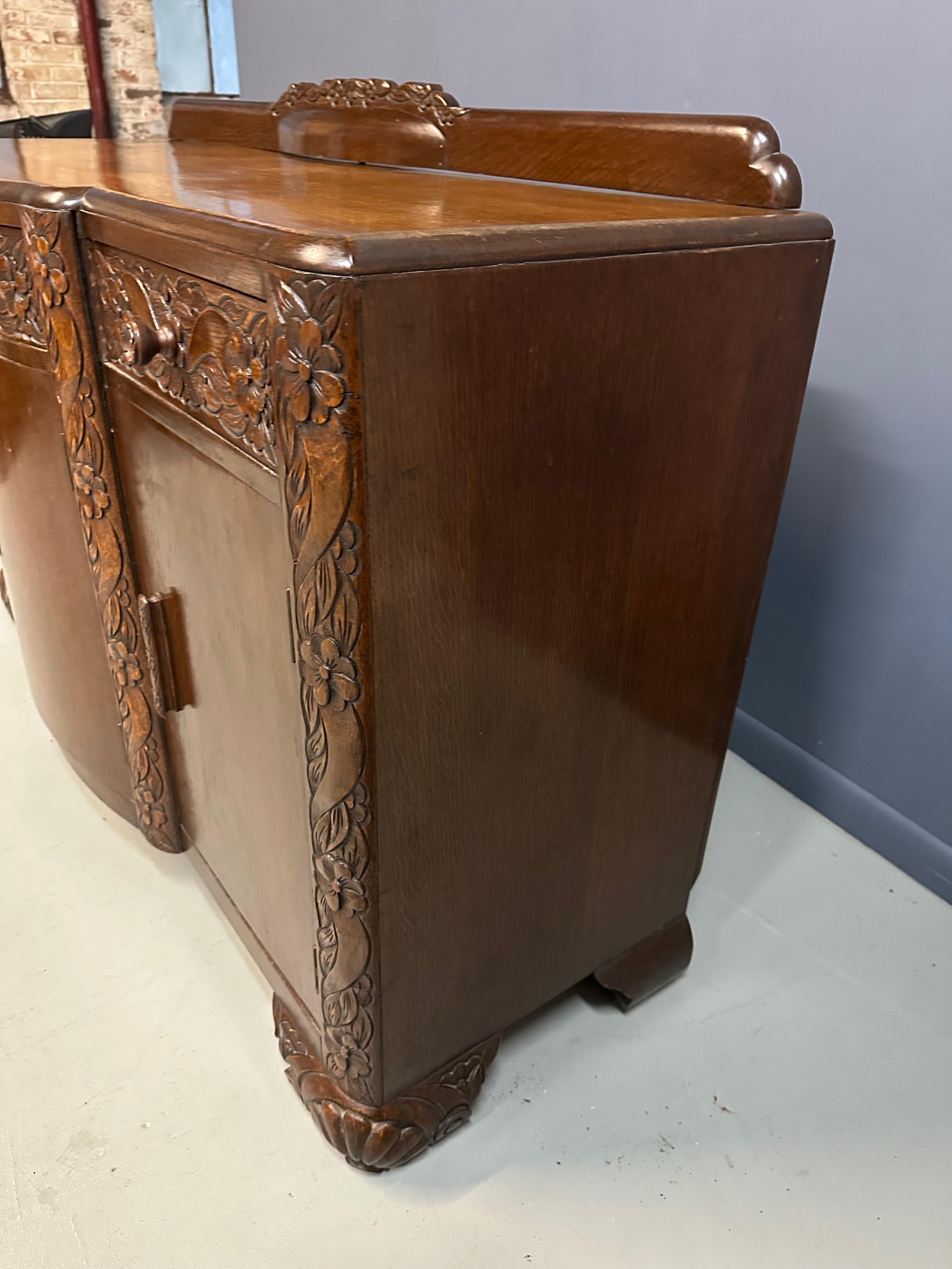 This rare 1920s English sideboard represents a late interpretation of Art Nouveau aesthetics, unusual for its period when Art Deco had largely supplanted earlier styles. Masterfully carved in solid oak, the piece features the sinuous organic lines