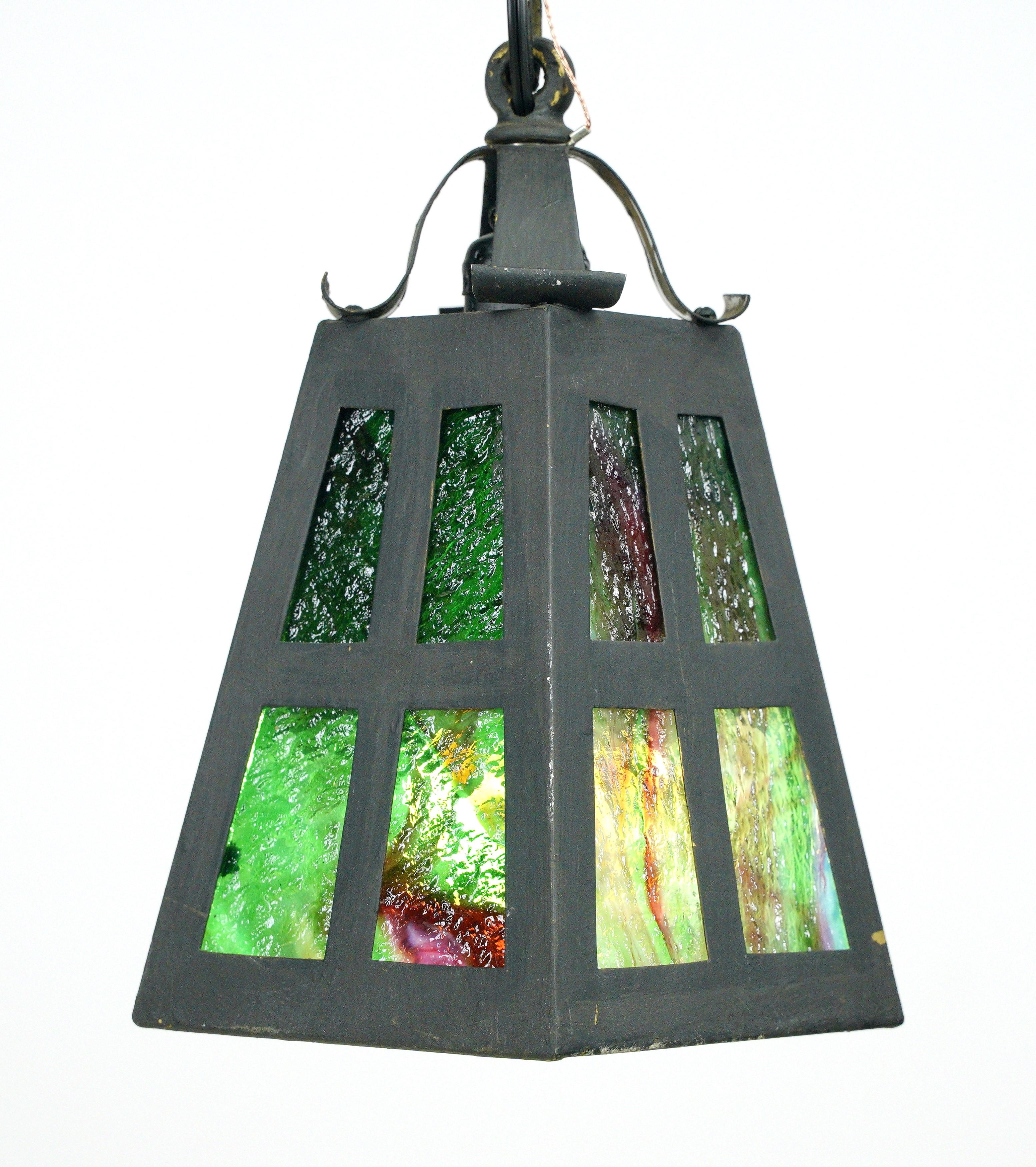 This pendant light has been carefully restored to its former glory, preserving the timeless design and craftsmanship of the 1920s. The fixture features stained glass panels in shades of green and yellow, creating a warm and inviting glow when lit.