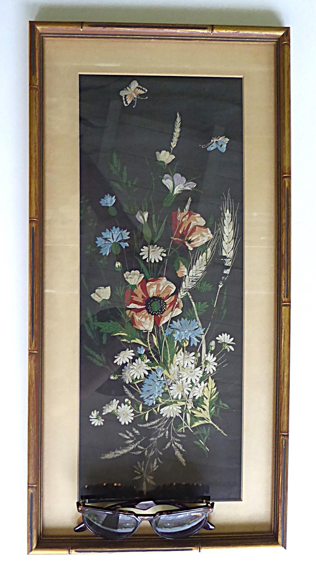 Bordado de principios del siglo XX probablemente enmarcado en la década de 1960 en un marco dorado de imitación de bambú. Bordado sobre fondo de seda negra de flores y vainas de trigo con dos mariposas en vuelo. El ramo incluye Amapolas rojas,