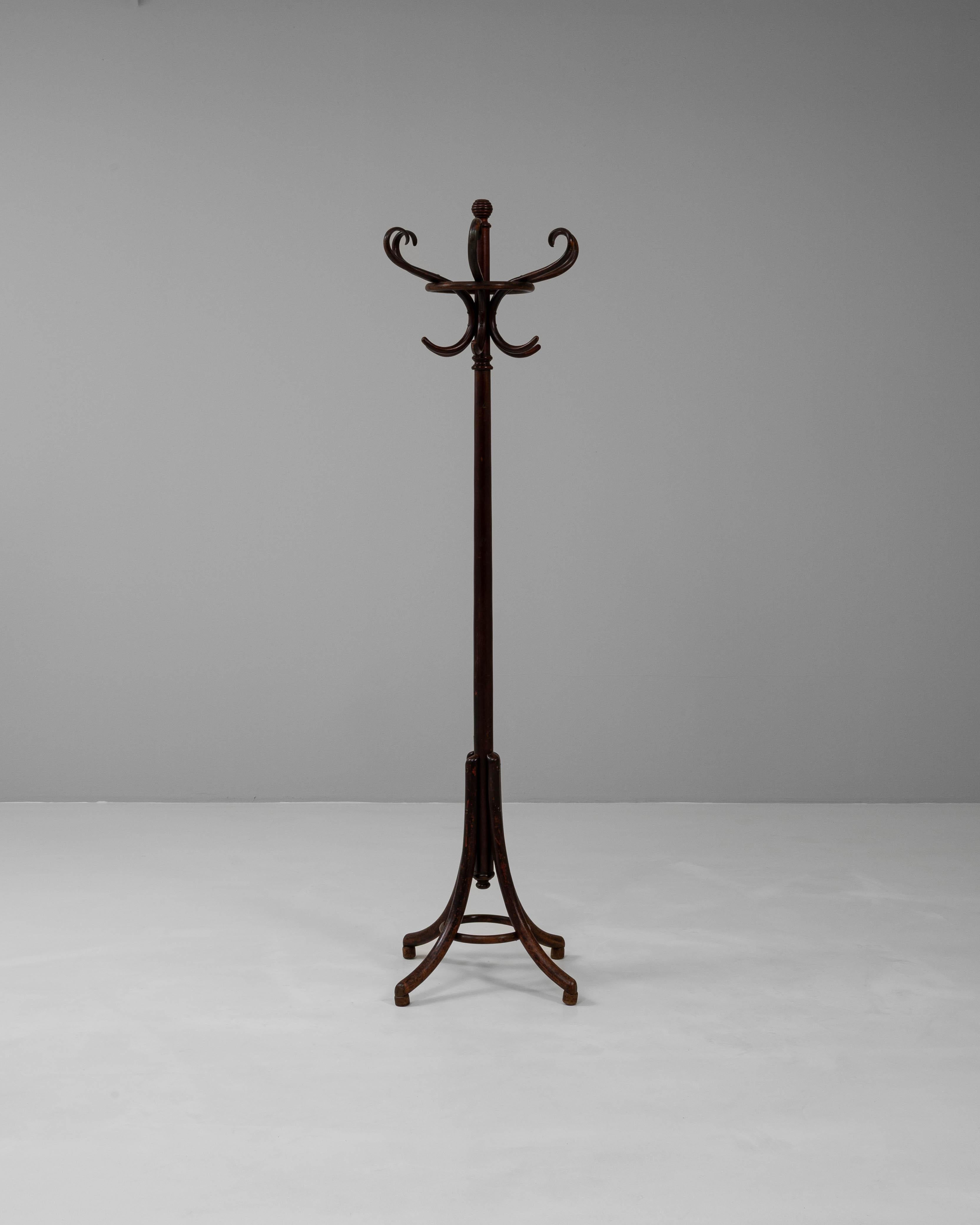 Este perchero austriaco de madera de los años veinte refleja la elegancia y funcionalidad del diseño europeo de principios del siglo XX. Fabricada en madera curvada siguiendo la tradición de Thonet, presenta una alta columna central rematada con