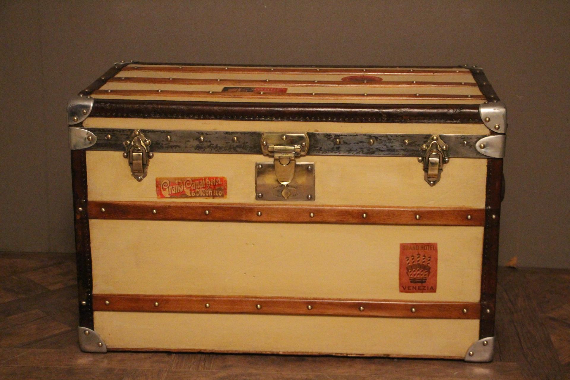 This nice steamer trunk features beige canvas, leather trim and side handles silver aluminum corners and brass locks.
A couple of travel labels.
Its main lock as well as its handle latches are marked 