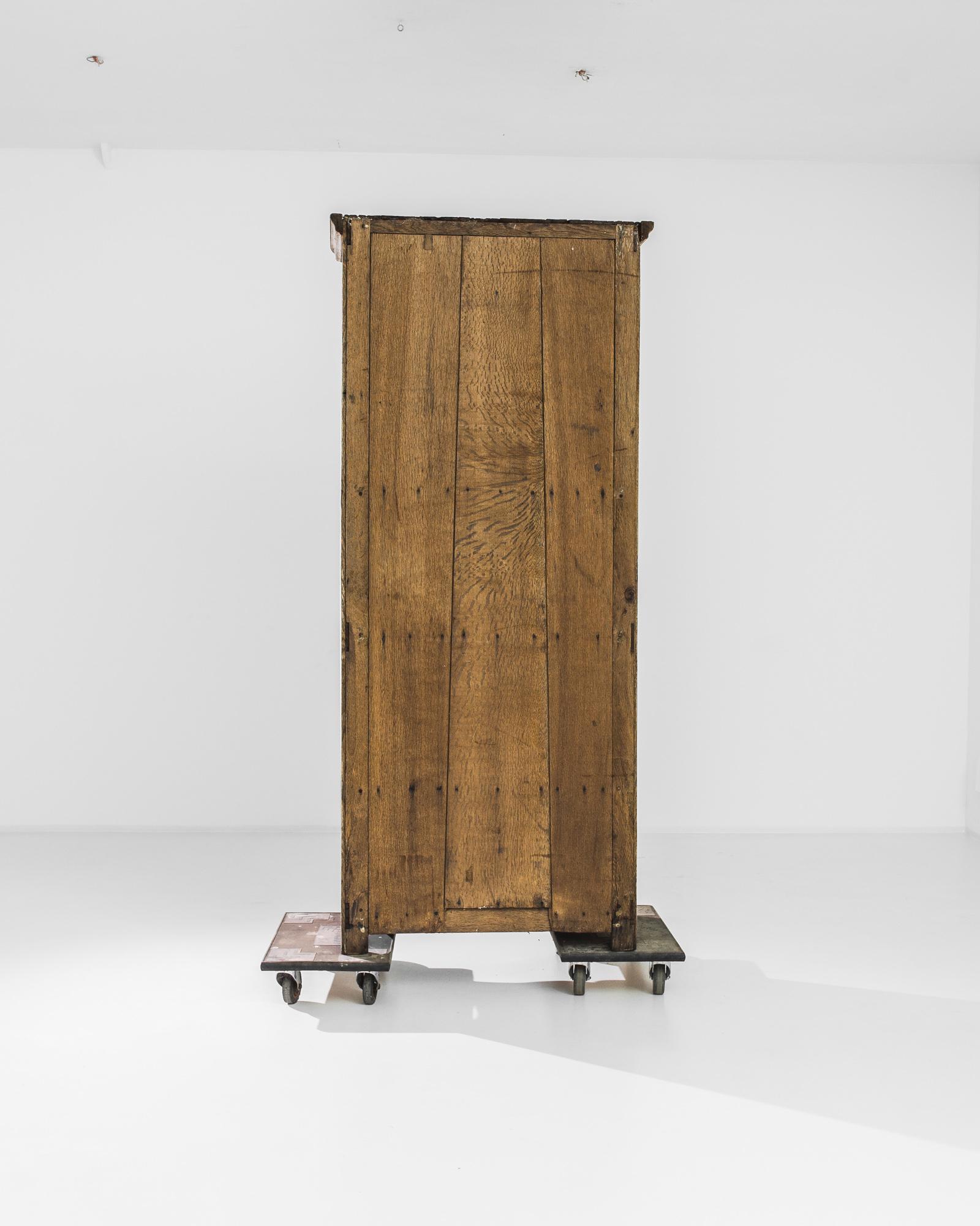 A vintage bleached oak cabinet from Belgium, produced circa 1920. This stately, tripartite chest stands tall at seven feet, featuring upper and lower locking cabinets with brass escutcheons, separated by a fold-down central section with six cubby