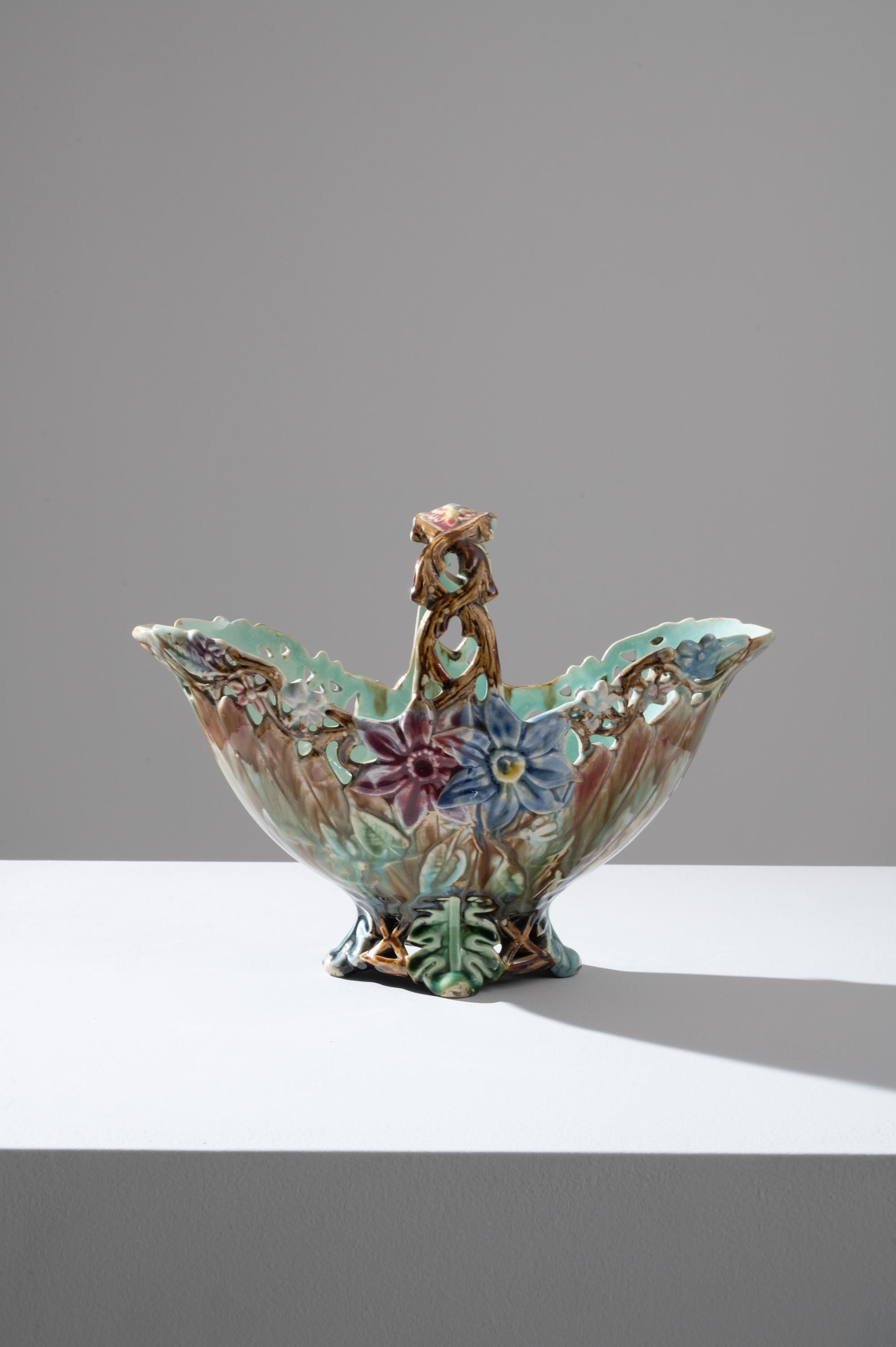 Delicate and whimsical, this vintage decorative ceramic bowl offers a woodland fantasy. Made in Belgium in the 1920s, the piece is shaped like a basket: but a basket composed of leaves, twigs and flowers, as if the plants of the forest had