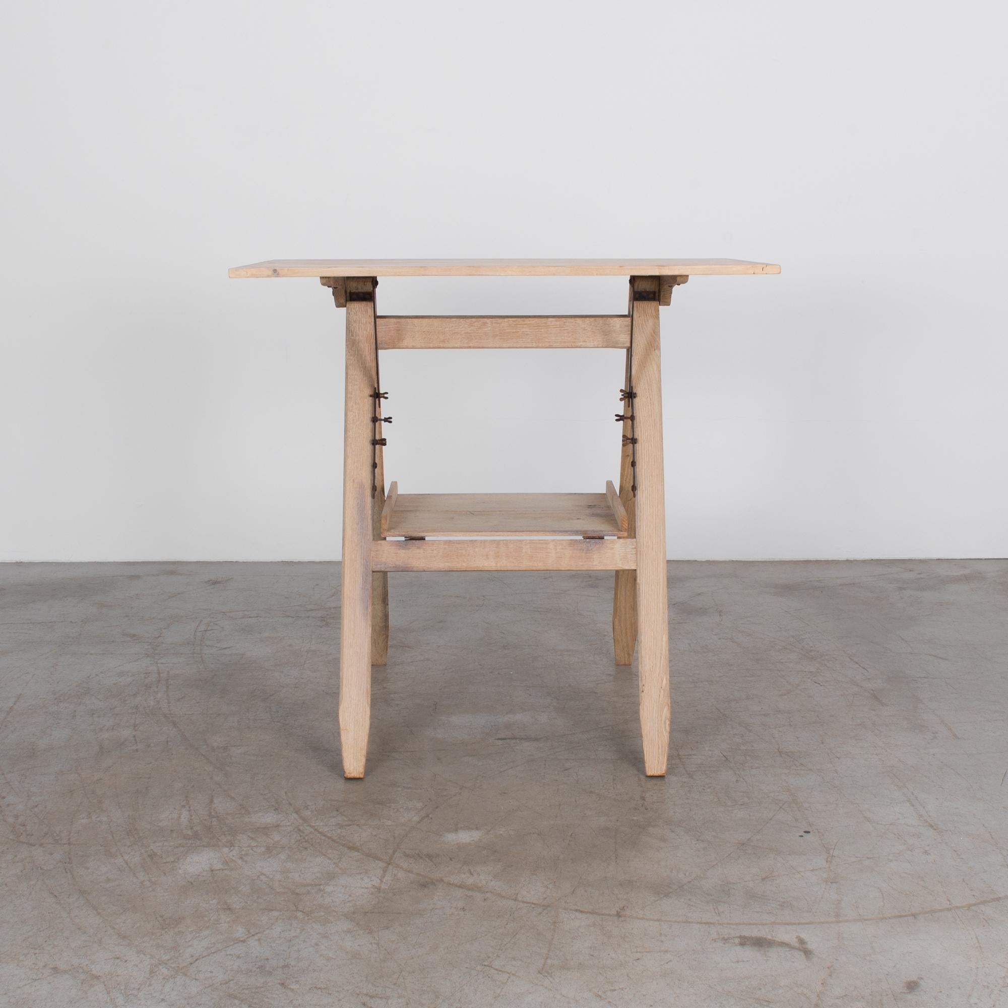 An adjustable drawing table from Belgium, circa 1920. This intriguing device is a standard period design featuring a beech wood table top and iron hardware. A minimal shape with oak table legs and an integrated storage shelf.