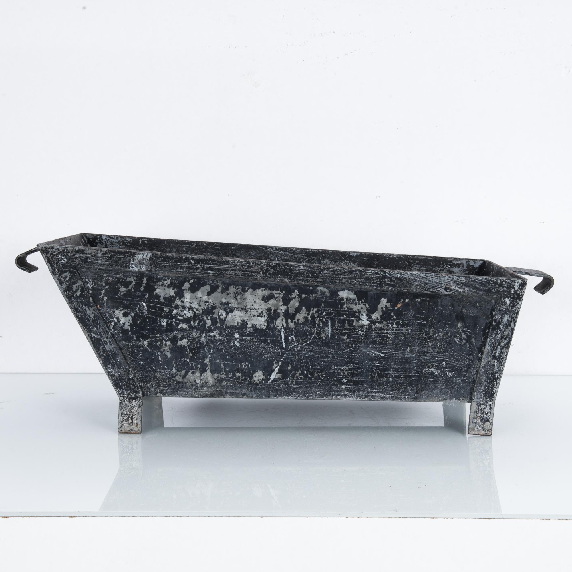 A zinc planter from Belgium, circa 1920s. A trough-like form with a worn, rustic finish. The original black paint contrasts with the zinc beneath. The tilted, asymmetric shape suggests an affectionate personality, emphasized by the distinctive