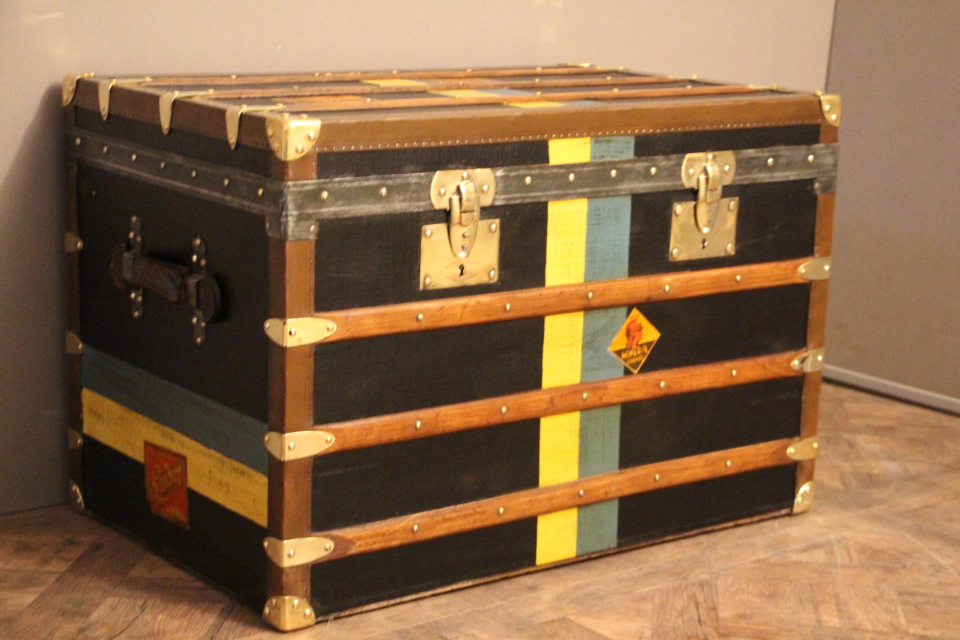 This nice steamer trunk features black canvas, leather trim and side handles and brass corners and locks.
Many travel labels and white yellow and blue stripes of customization.
Its locks as well as its handle latches are marked 