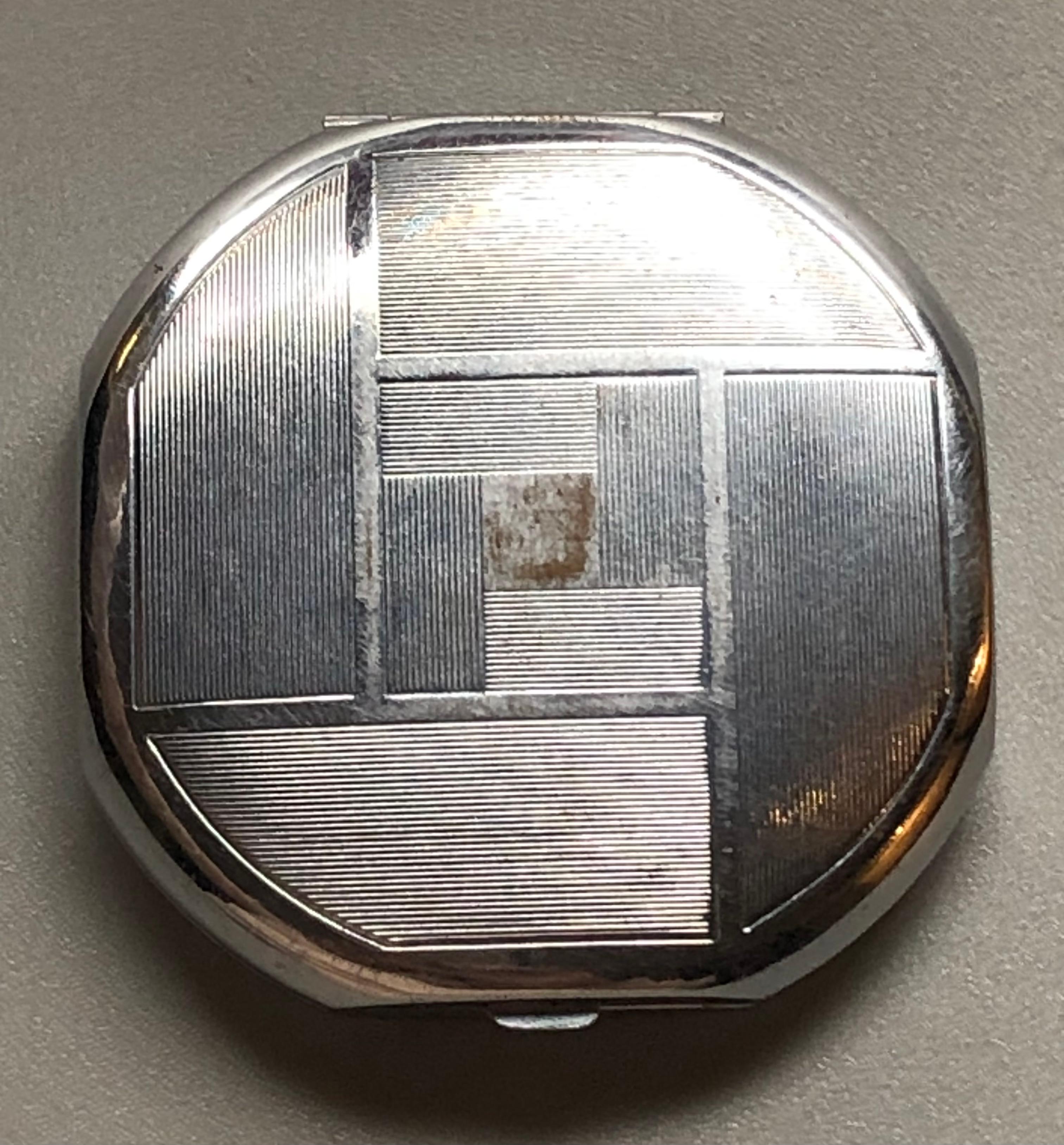 This beautiful round compact has squared off edges, the enamel is in an unusual duck egg blue and a contrasting deeper blue on the front, being completed by a silver square swirl pattern in the centre. The base has a mirrored image of the front in a