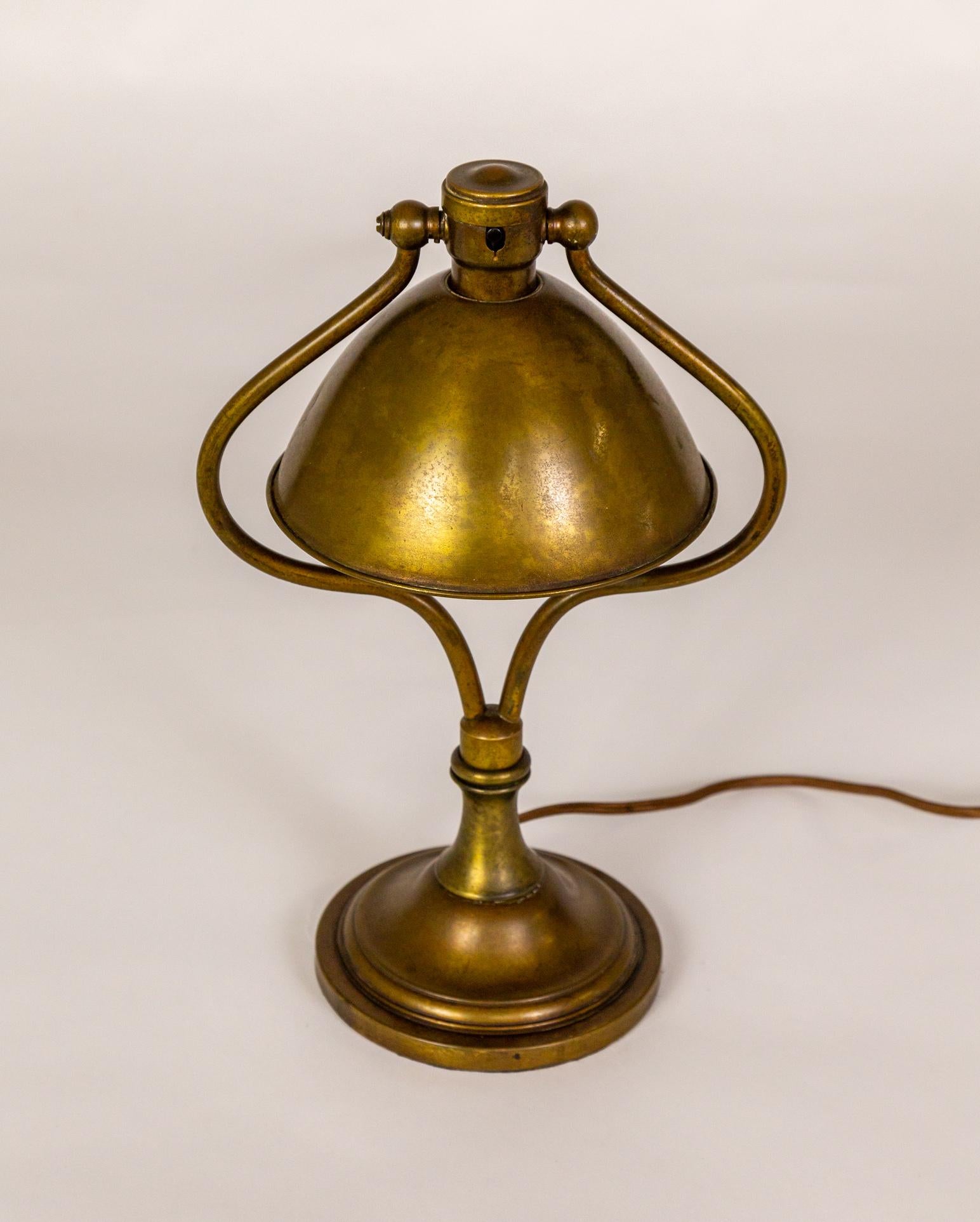 An Arts & Crafts brass harp desk/table lamp. Finely crafted by Bradley & Hubbard in the early 20th century, this lamp is a great task light with a swing shade for directional illumination. It has a weighted base and is newly rewired with the