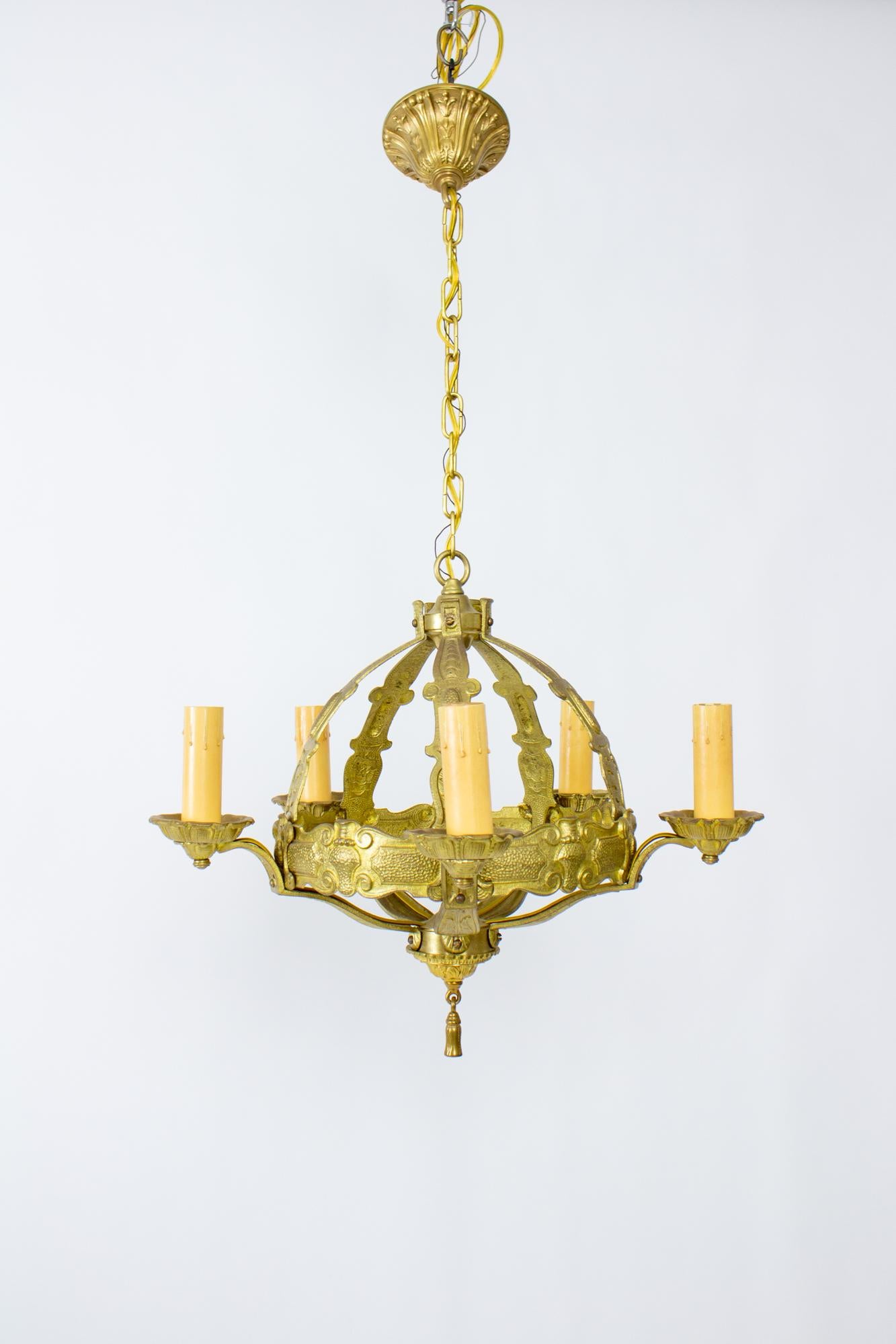 1920’s brass gothic revival chandelier with five arms, also can be referred to as tudor style. This chandelier is solid cast brass with a cage form and central roped stem. The five arms are cups that extend from the central orb or the cage. Brass
