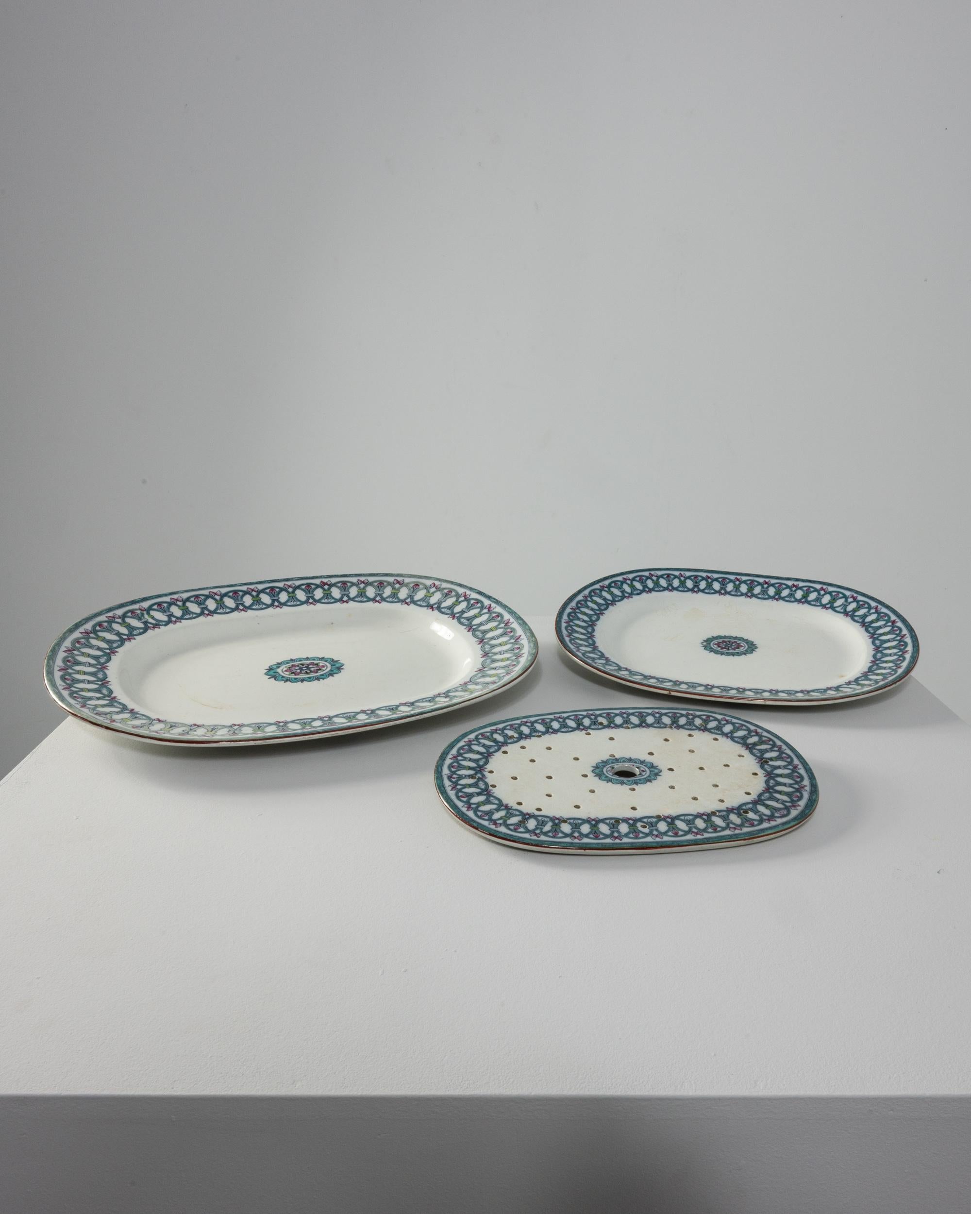 This elegant set of vintage ceramic plates includes two serving dishes and a perforated platter —a rare piece which was intended to collect the juices from a freshly cooked piece of meat as it was being served. Made in Britain in the 1920s, the