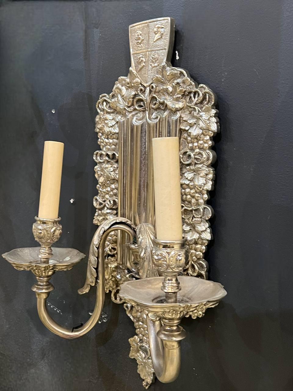 A pair of circa 1920’s Caldwell neoclassic style silver plated engraved sconces with two lights. Grapes on shield design