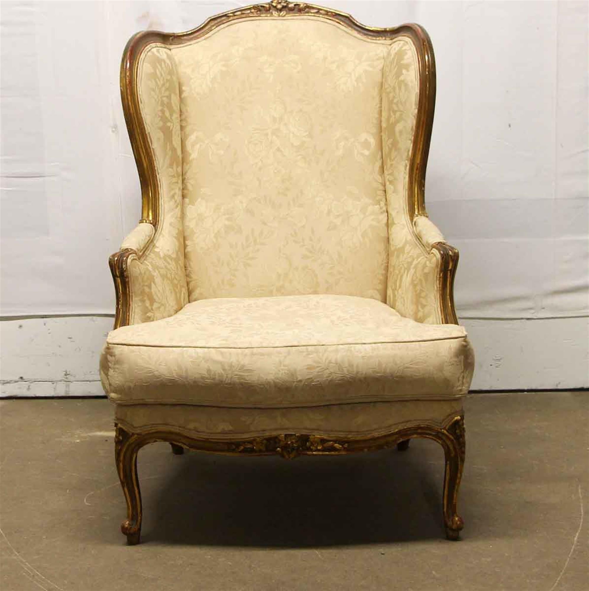 19th century wing back chair with cream colored floral and ribbon upholstery and a carved floral wooden frame. There is general wear from age and use. This can be seen at our 400 Gilligan St location in Scranton, PA.