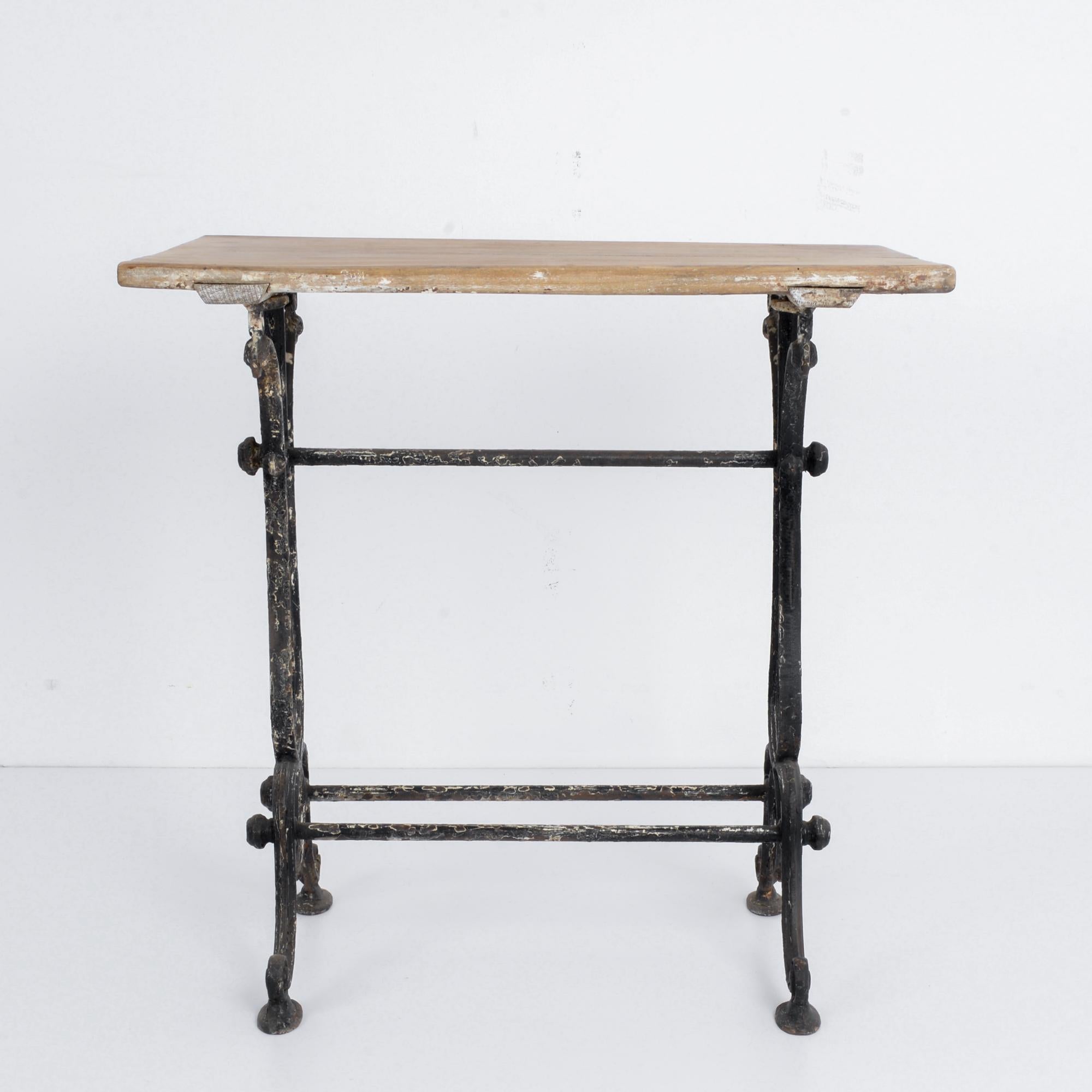 This bistro table with a cast iron frame and wooden tabletop was made in France, circa 1920. The horizontal lines of the table and stretchers highlight the elegant, curvilinear table legs. The table features a timeworn patina, evoking the bustle and