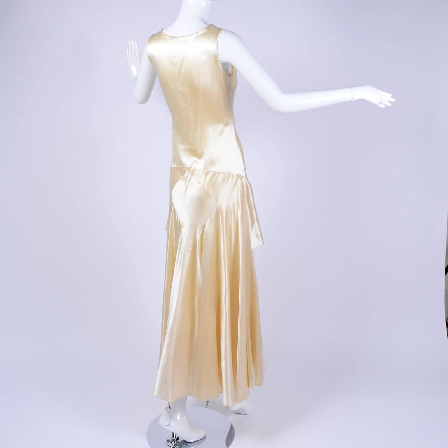 This is a late 1920's vintage wedding dress in a champagne silk slipper satin. The dress is sleeveless with a ruffle that stars at the hips, side snaps and matching fabric sash. We estimate this dress to fit a modern day size 4 but please use the