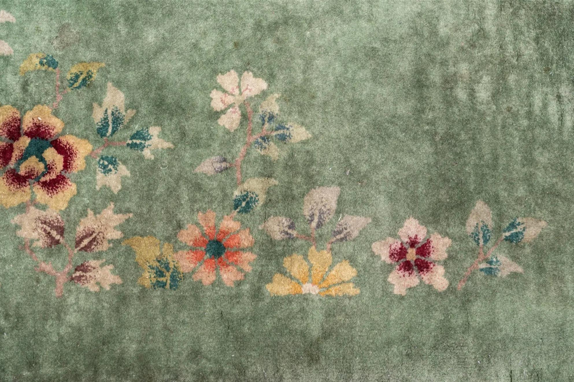 Tapis en laine de l'usine chinoise Nichols, avec un motif floral dispersé. Affichant plusieurs couleurs, les fleurs sont situées sur les deux longues bordures. Une étiquette est située sous la bordure du tapis.