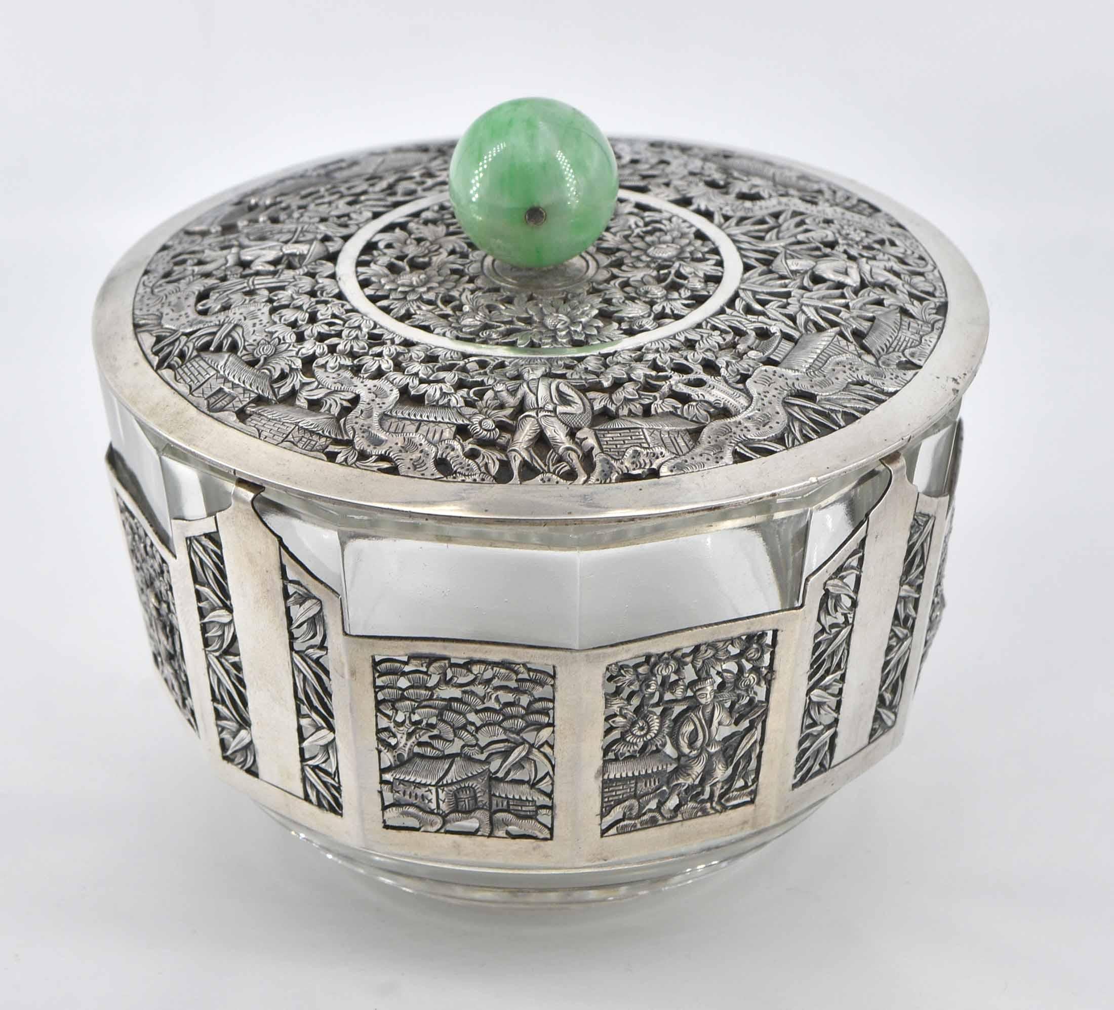 A 1920's Chinese silver mounted lidded bowl with jade turned handle.

The silver plate has lovely pierced scenic decoration, with a step-form glass base inner.

There is some rubbing with age, and a small loss of silver plate which is visible