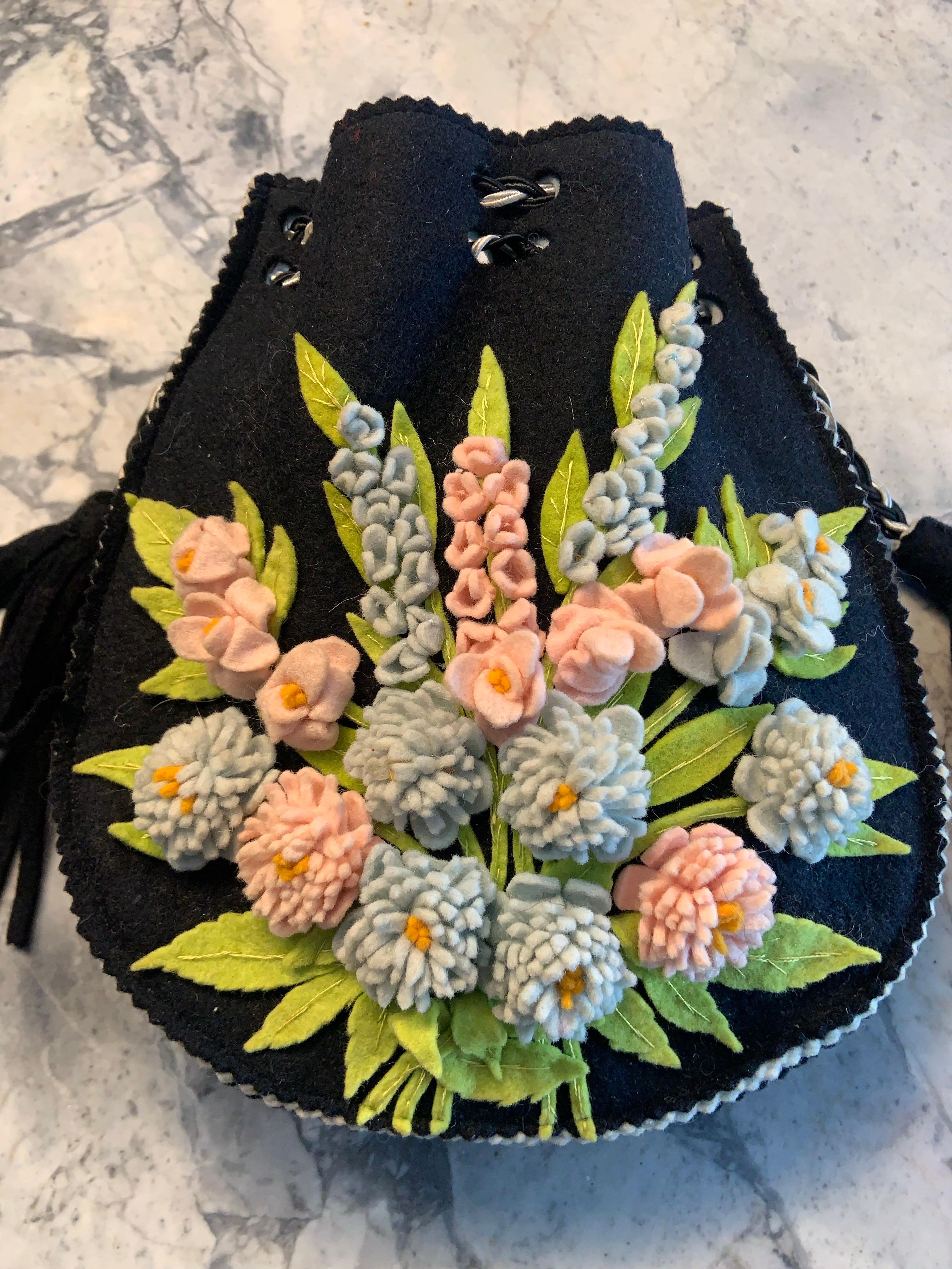 Ce sac à main des années 1920 est tellement impeccable qu'on pourrait croire qu'il a été fabriqué hier et non il y a 100 ans. Le sac est fabriqué en feutre noir et décoré de fleurs roses et bleues en feutre brodées à la main et de feuilles vertes en