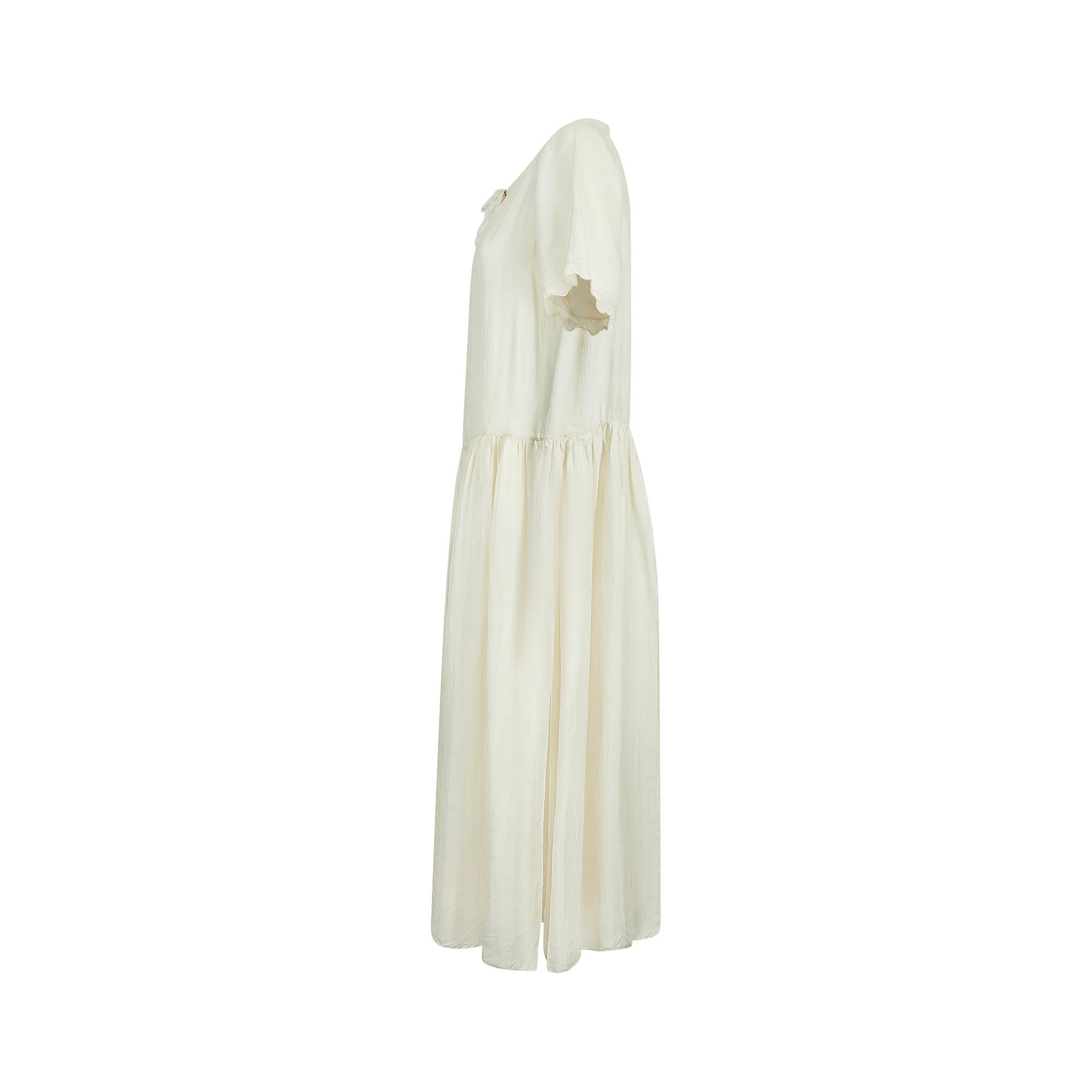 This enchanting antique wedding dress is in wonderful condition for a piece of its age and delicacy. Designed a century ago, it is crafted from fine cream silk in the laid-back apron style that was the early 1920s vogue. The fluid cut and drop-waist