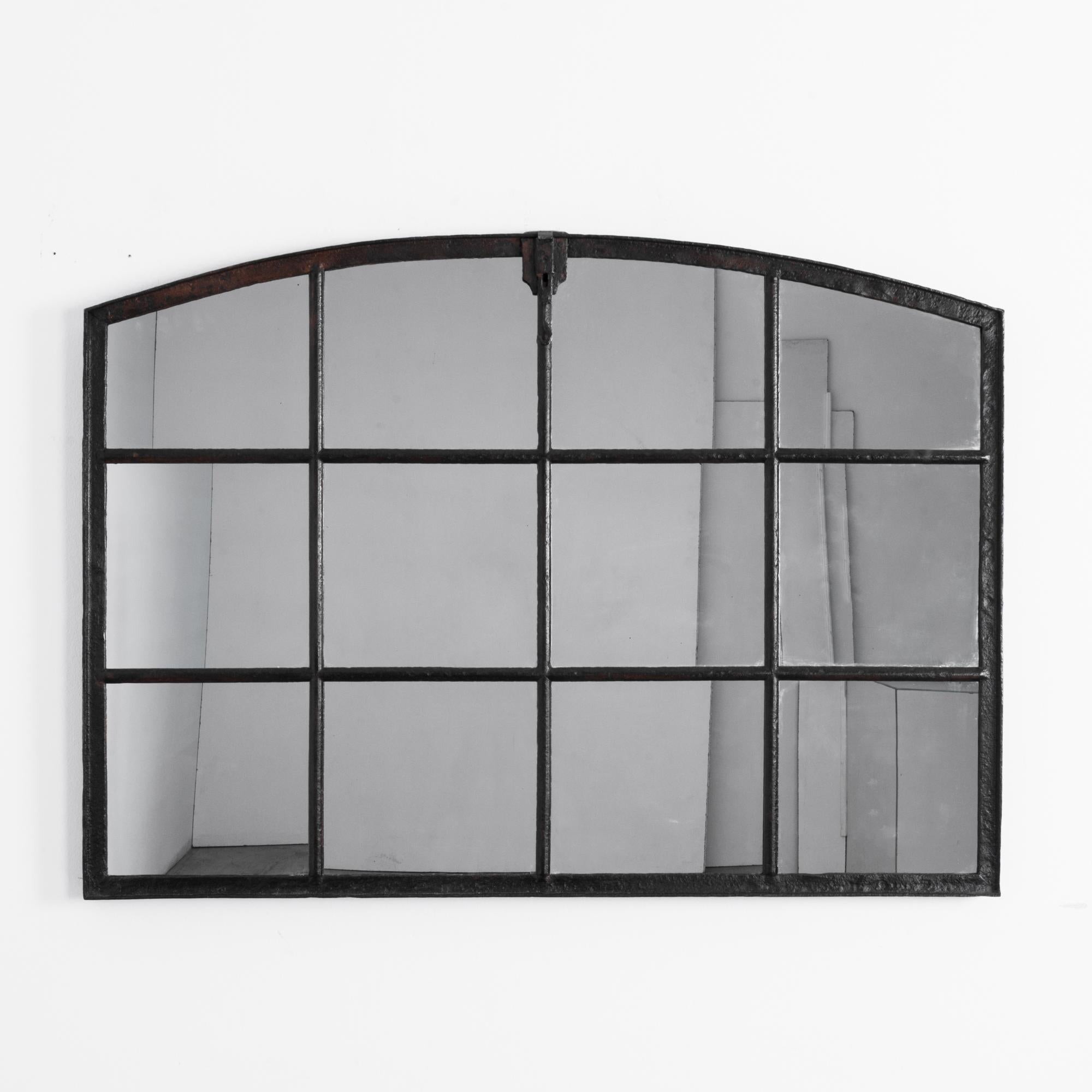 A mirrored factory window from Czechia, circa 1920. A wide mirror is sustained by a grid of cast metal. The dark color and sheer weight of the frame give this mirror an impressive presence, softened by a gentle arch. A striking post-industrial piece