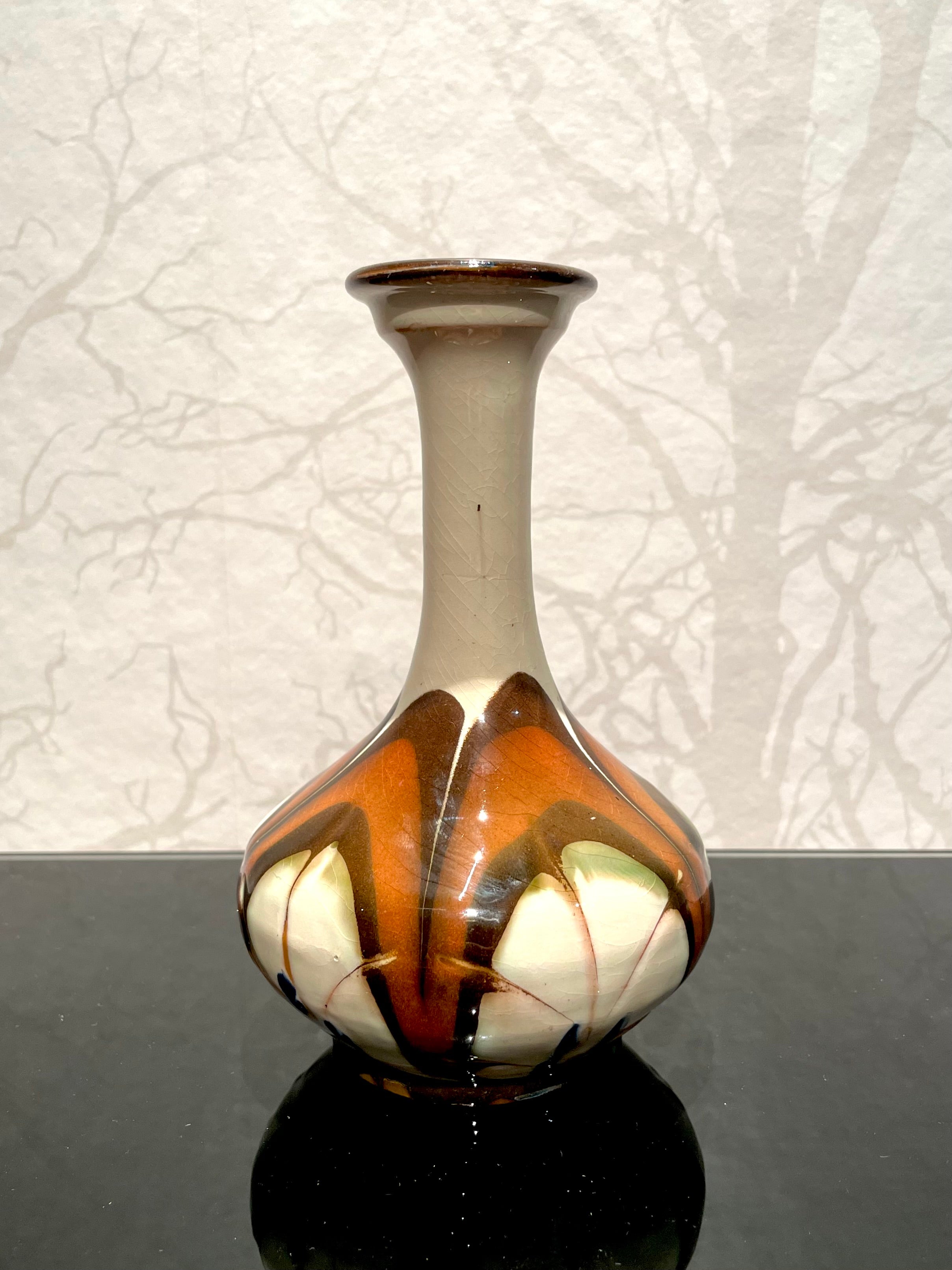 This is a 1920s Danish 16.5 cm high necked ceramic vase by Herman Kähler. 

It comes with a baluster shaped body. It has a glossy surface, cow horn glazed pattern like flowers. Brown and green colors on a creamy white background with forget-me-not