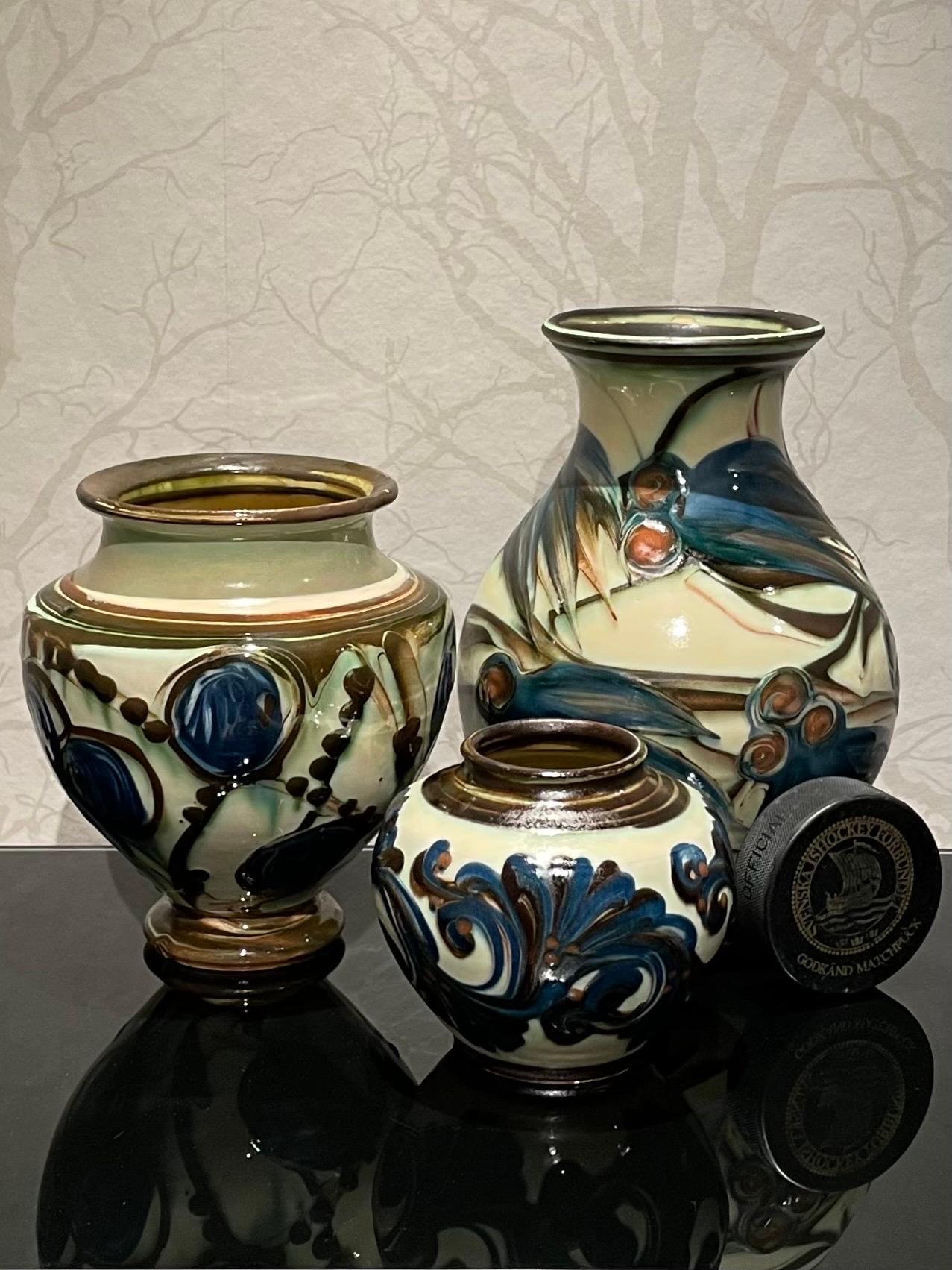 This is the 1920s Danish 3 vases collection by Herman Kähler. 
It comes with baluster shaped body’s, high to medium glossy surface and deep brown and royal blue colors on a cream white base. 
They all have a beautiful cow horn glazed pattern of