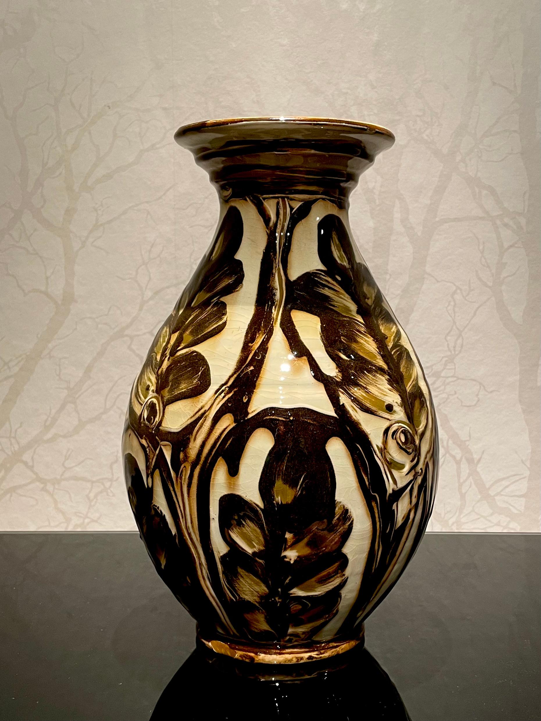 This is the 1920s Danish xx cm high ceramic vase by Herman Kähler. 
It comes with a baluster shaped body, high glossy surface and warm, very deep brown and green color on a cream white base. 

The pattern, consisting of branches and leaves, creates
