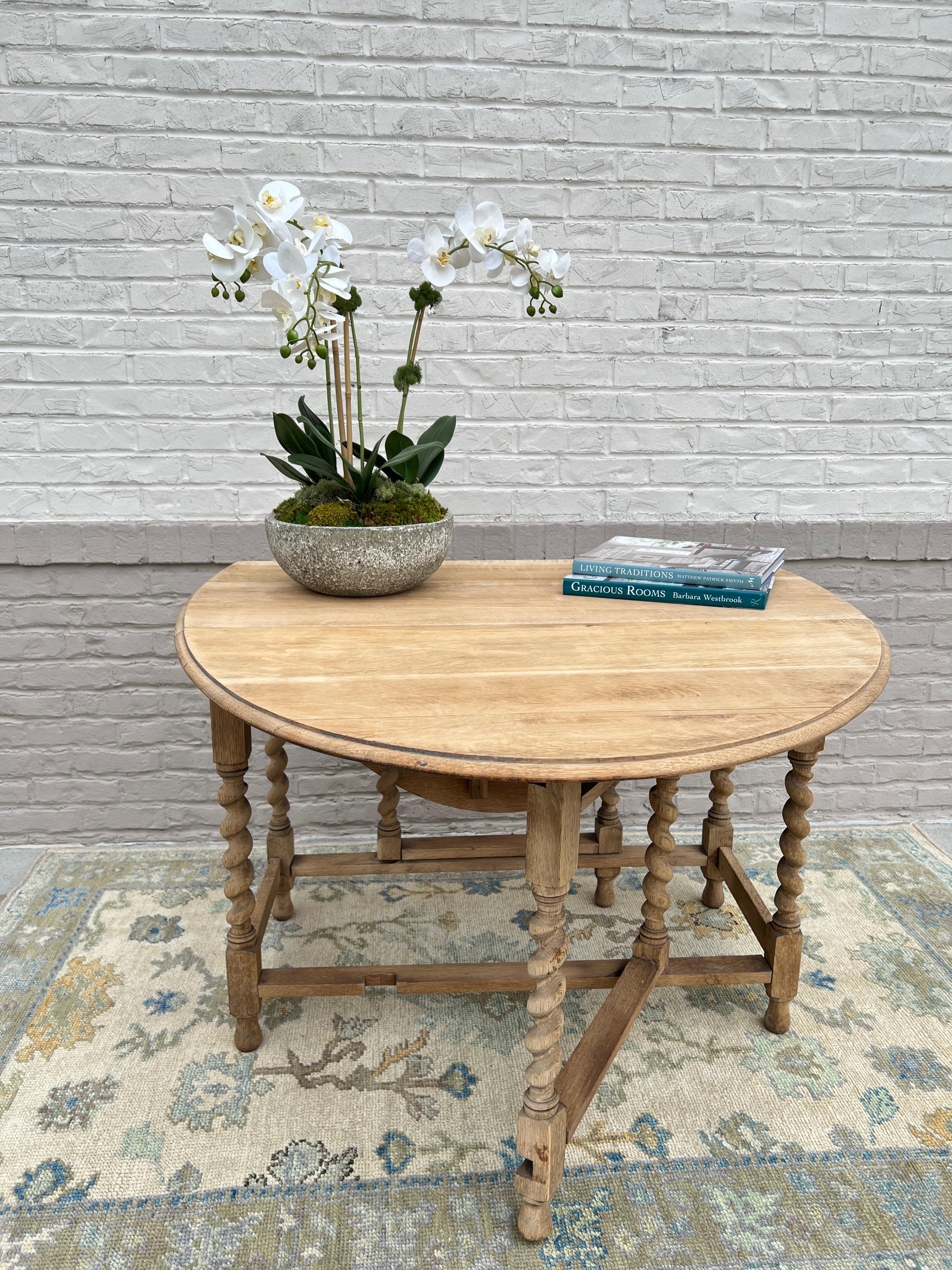 circa 1920s England. 
A gorgeous bleach oak folding gateleg table, filled with old-world charm. The carved details and turned table legs highlight its beauty. The sides of the circular table fold down, allowing it to be easily stored when not in