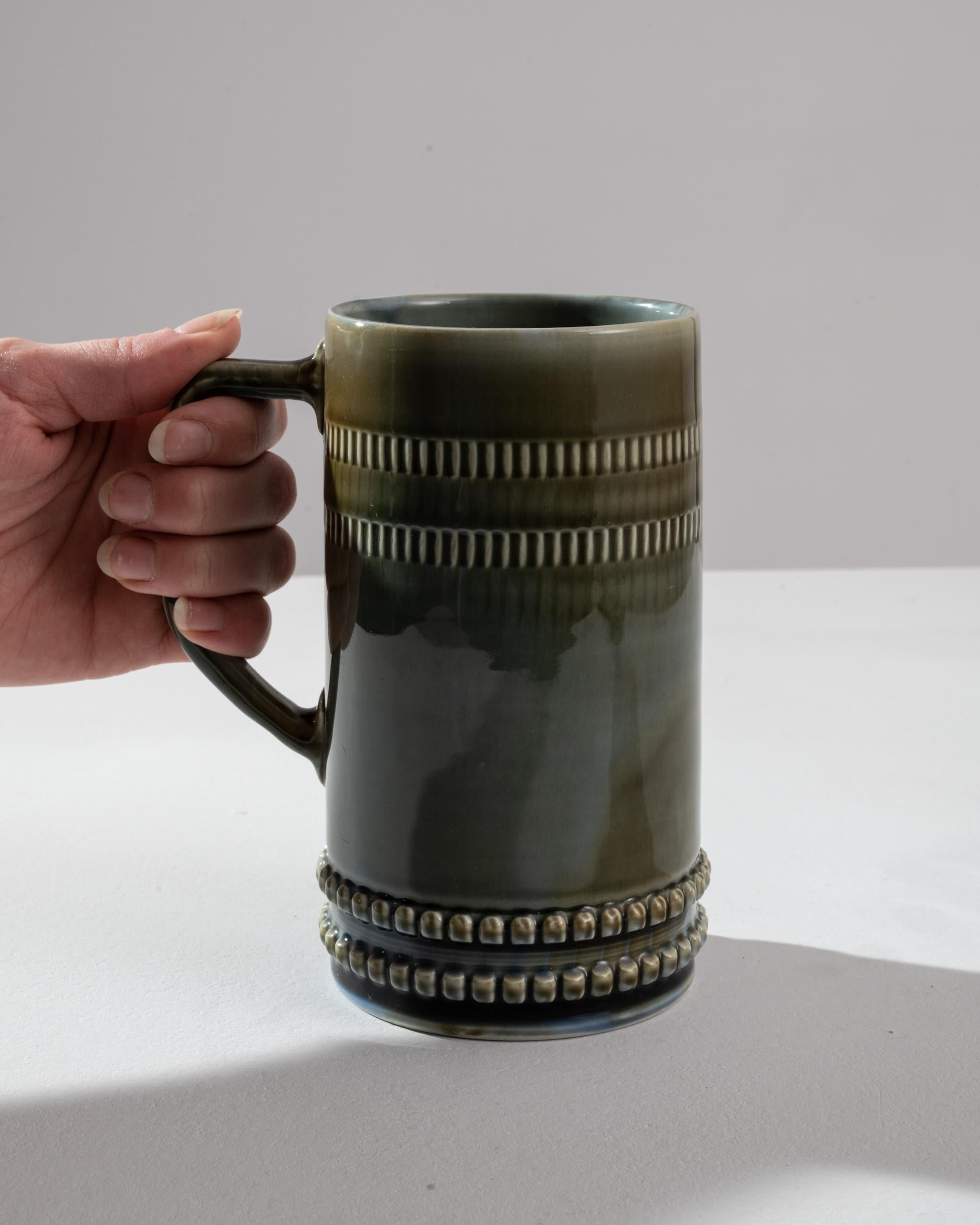 Indulge in the vintage charm of this 1920s European Ceramic Tankard. Crafted in a mesmerizing blue-green ceramic, it exudes a sense of timeless elegance. The tankard boasts beautiful designs that add to its allure, showcasing the craftsmanship of a