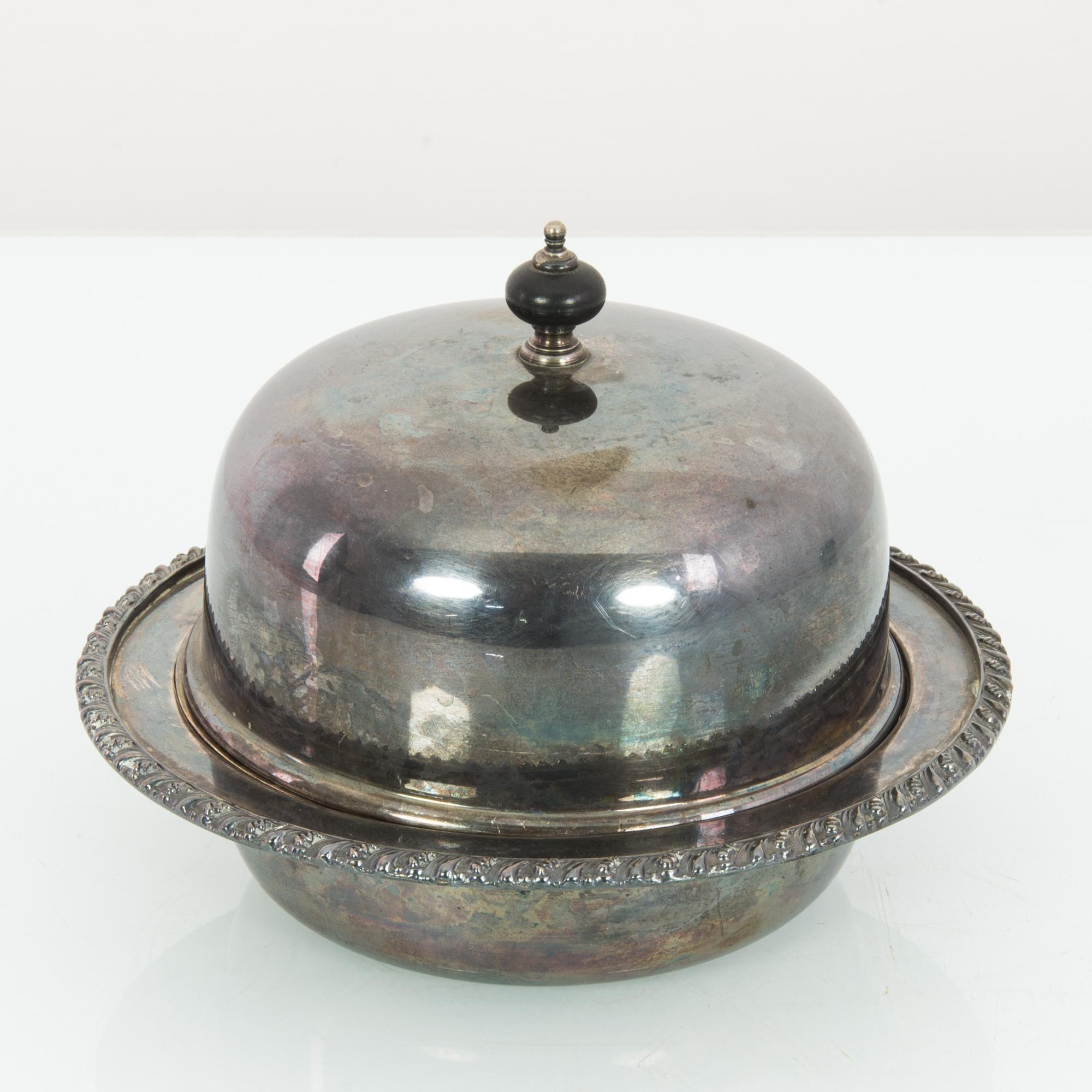 This silver-plated serving bowl with an insert was made in Europe, 1920. It features a carved rim, and its lid is topped with a globe finial. With its timeworn patina, this serving bowl will bring a touch of elegance from yesteryear.