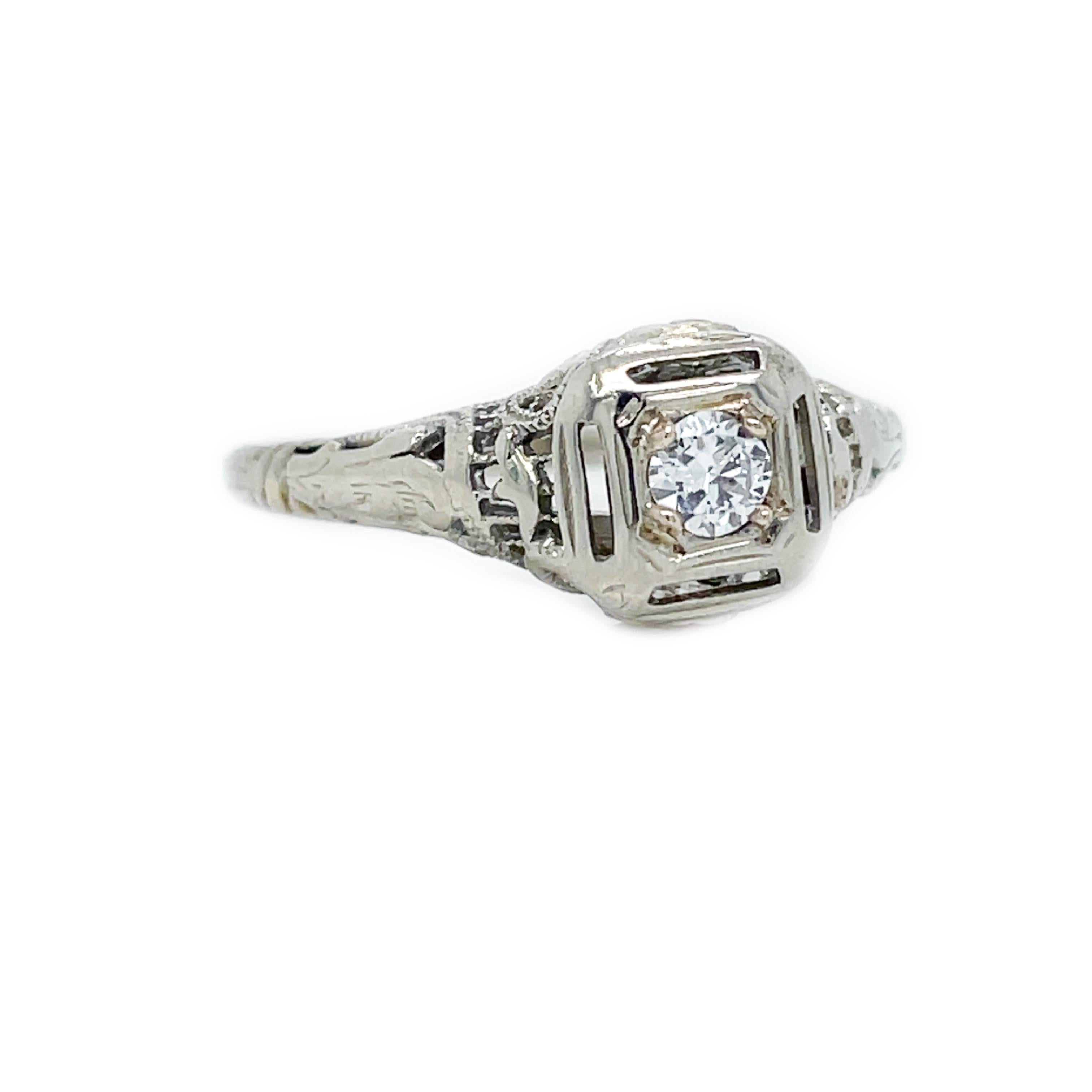 This is a gorgeous 18K white gold filigree ring from the 1920s showcasing a gorgeous white diamond at its center! A bright-white and sparkling round diamond, weighing .15 carat, scintillates within a double square setting, detailed with fine