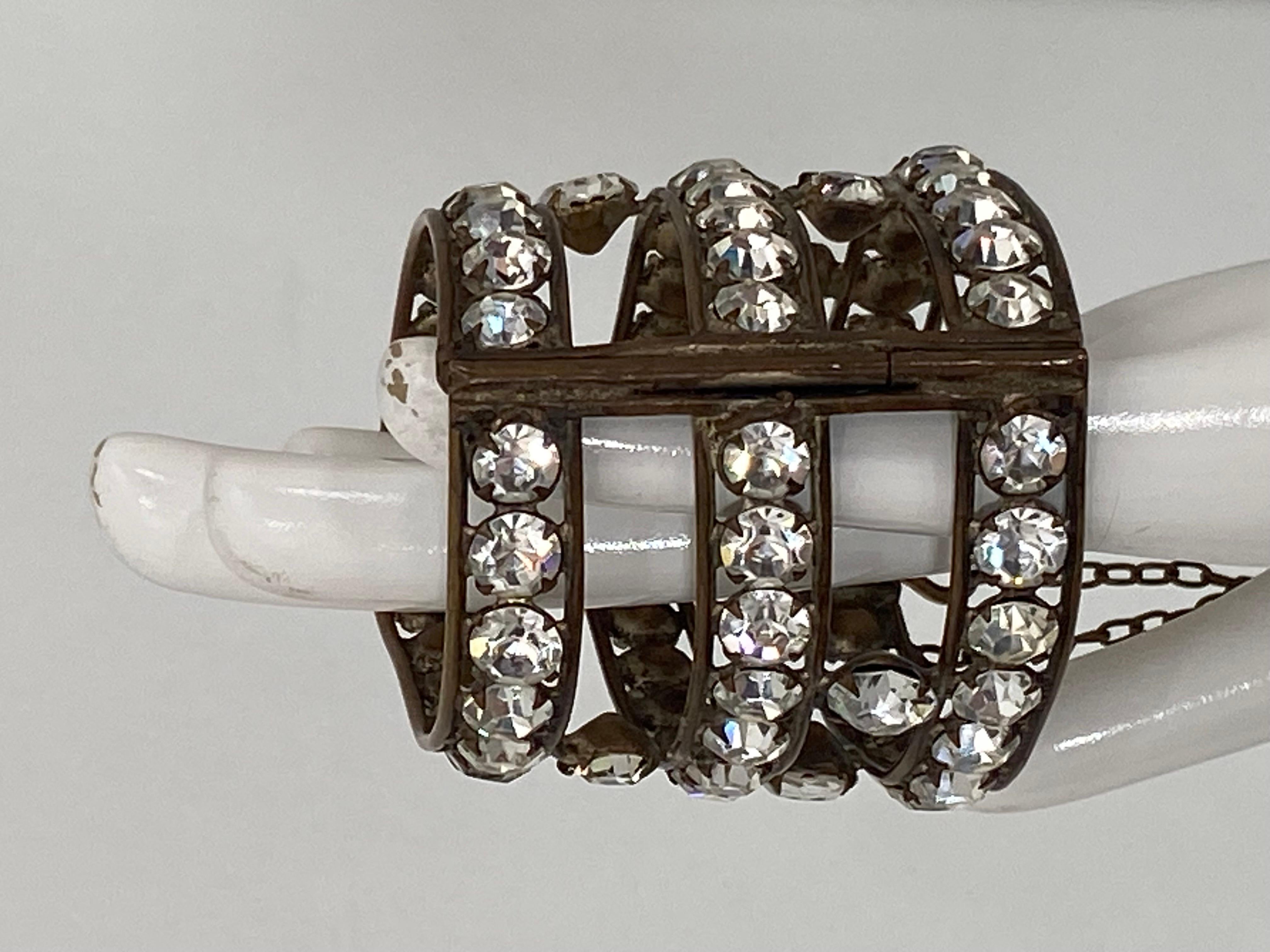 1920s flapper costume, open work brass frame cuff bracelet with large sparkly prong set rhinestones. The bracelet is oval and narrow at the opening near the hand & wider at the opening up your arm. Opens and closes at the side with a long pin that