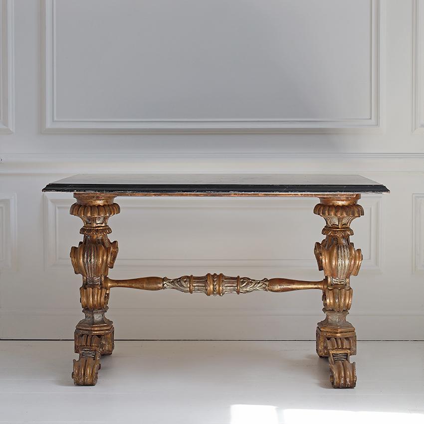 A refined 17th-century inspired Florentine table featuring intricately carved legs and a central stretcher bar, circa 1920. The hand-painted marble-effect top adds a layer of artistry to its classic silhouette, echoing the elegance of Jacobean and