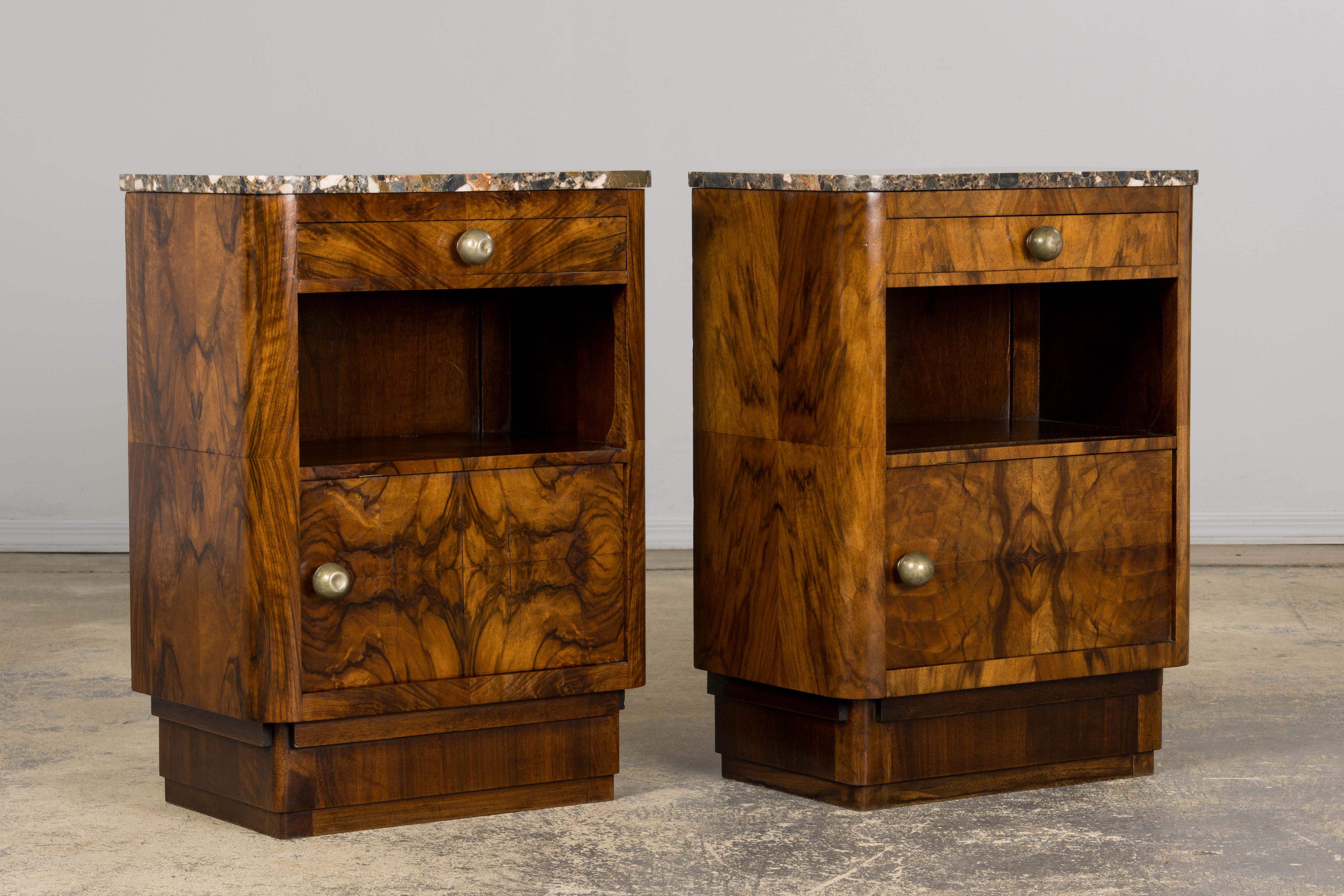 A refined pair of 1920s French Art Deco nightstands or side tables, sourced in Paris. Handcrafted from solid walnut and topped with beautifully veined marble in gray and earthy tones, each piece reflects the elegance and symmetry of the Art Deco