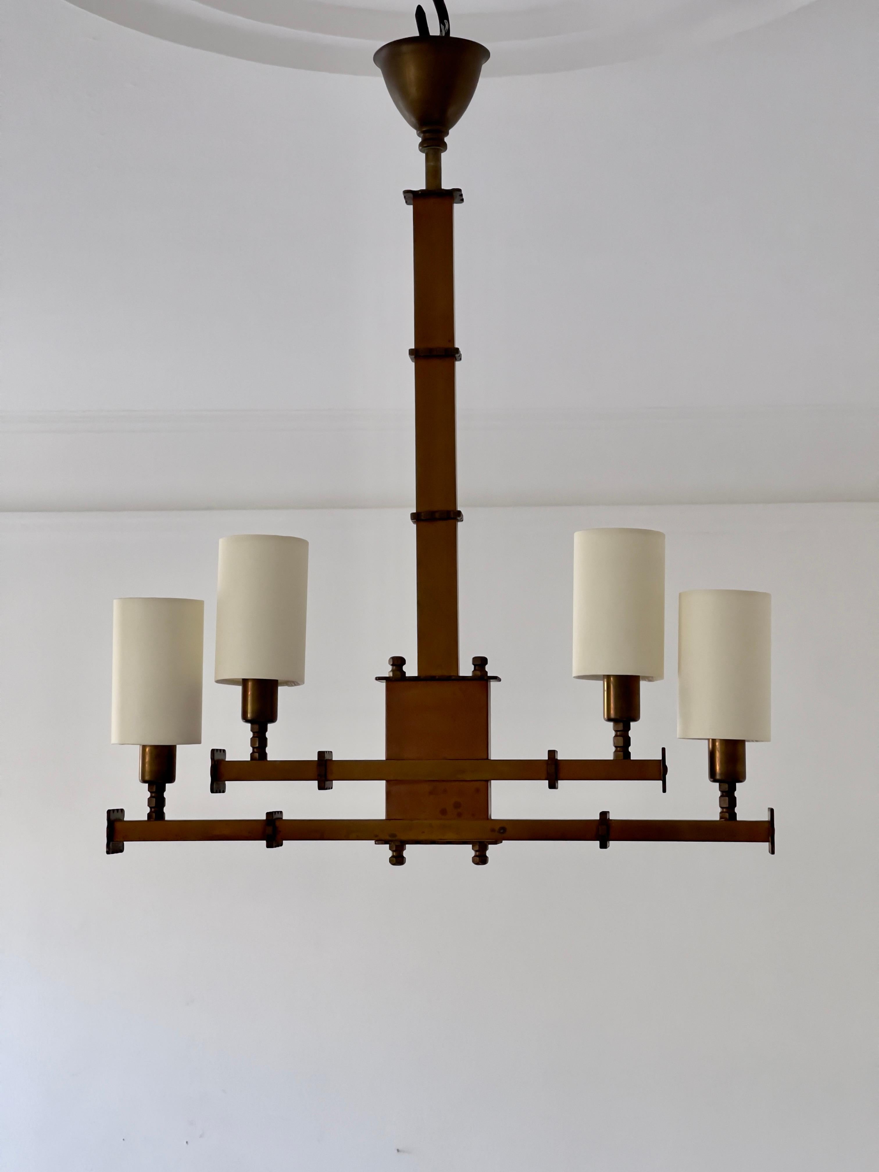 Rare 20th century french Art Deco chandelier in beautiful patinated brass and new original reconstructed shades of raw silk. The solid brass construction and rhythmic structures speaks the language of brutalism and also resonates the architectural