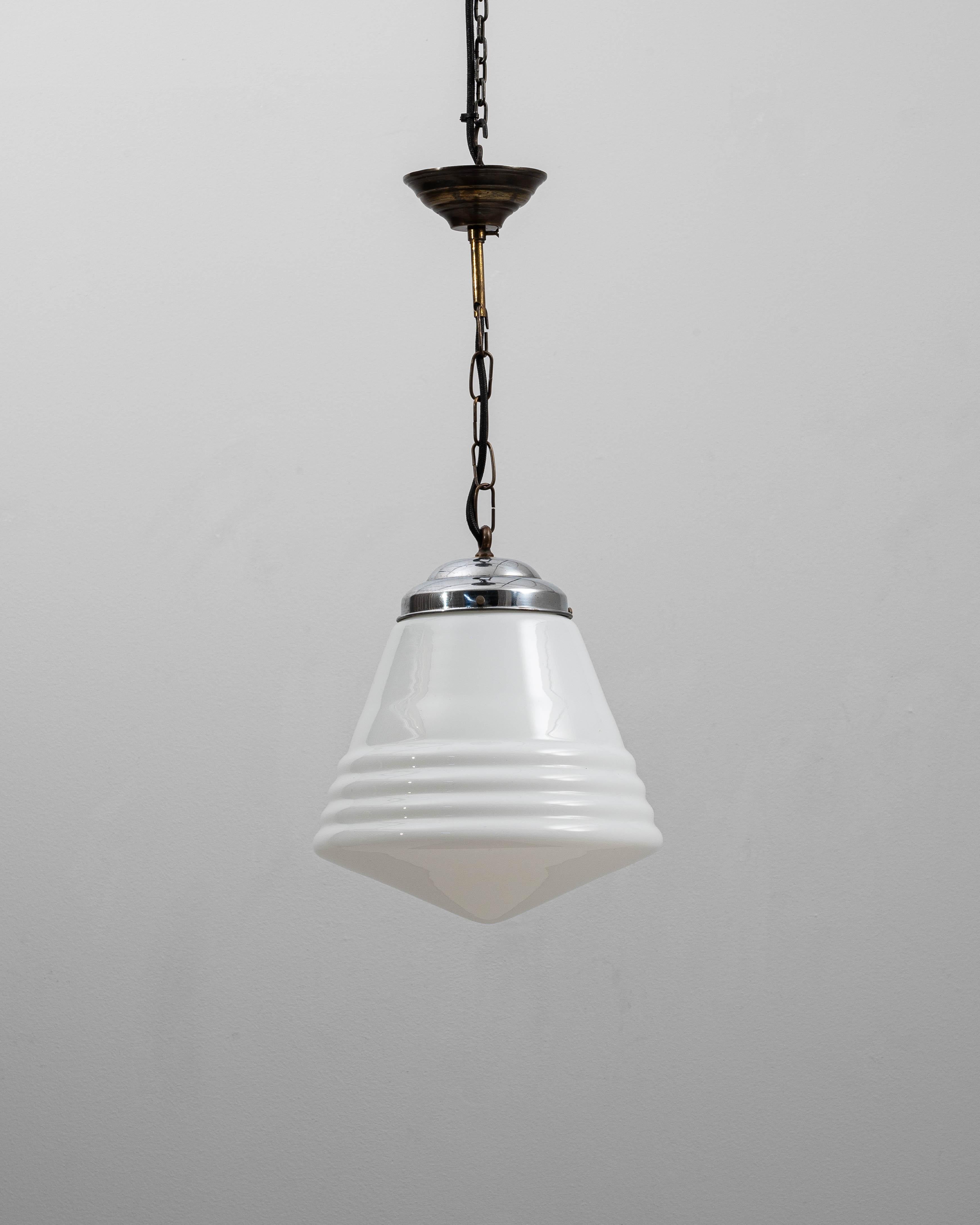 This 1920s French Art Deco glass pendant exemplifies the movement’s emphasis on bold geometry and refined materials. The opaline glass shade features a striking tiered design, with a stepped midsection that adds architectural rhythm and diffuses