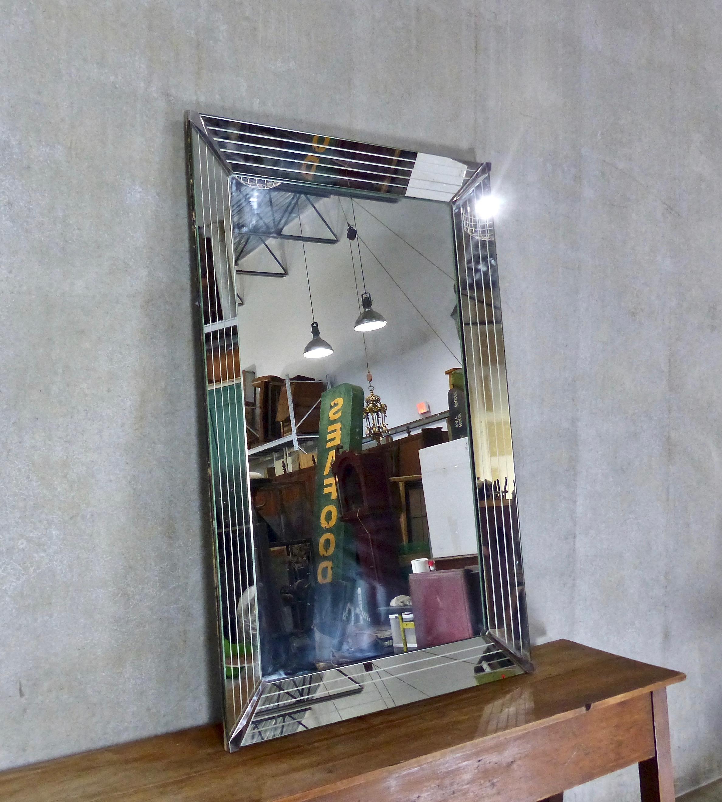 A large French mantel mirror in beautiful Art Deco style. Original mirror surfaces over solid wood. Deeply angled frame (also mirrored) features classic pinstripe details along with “chevron” style corner brackets.
Dimensions: 60