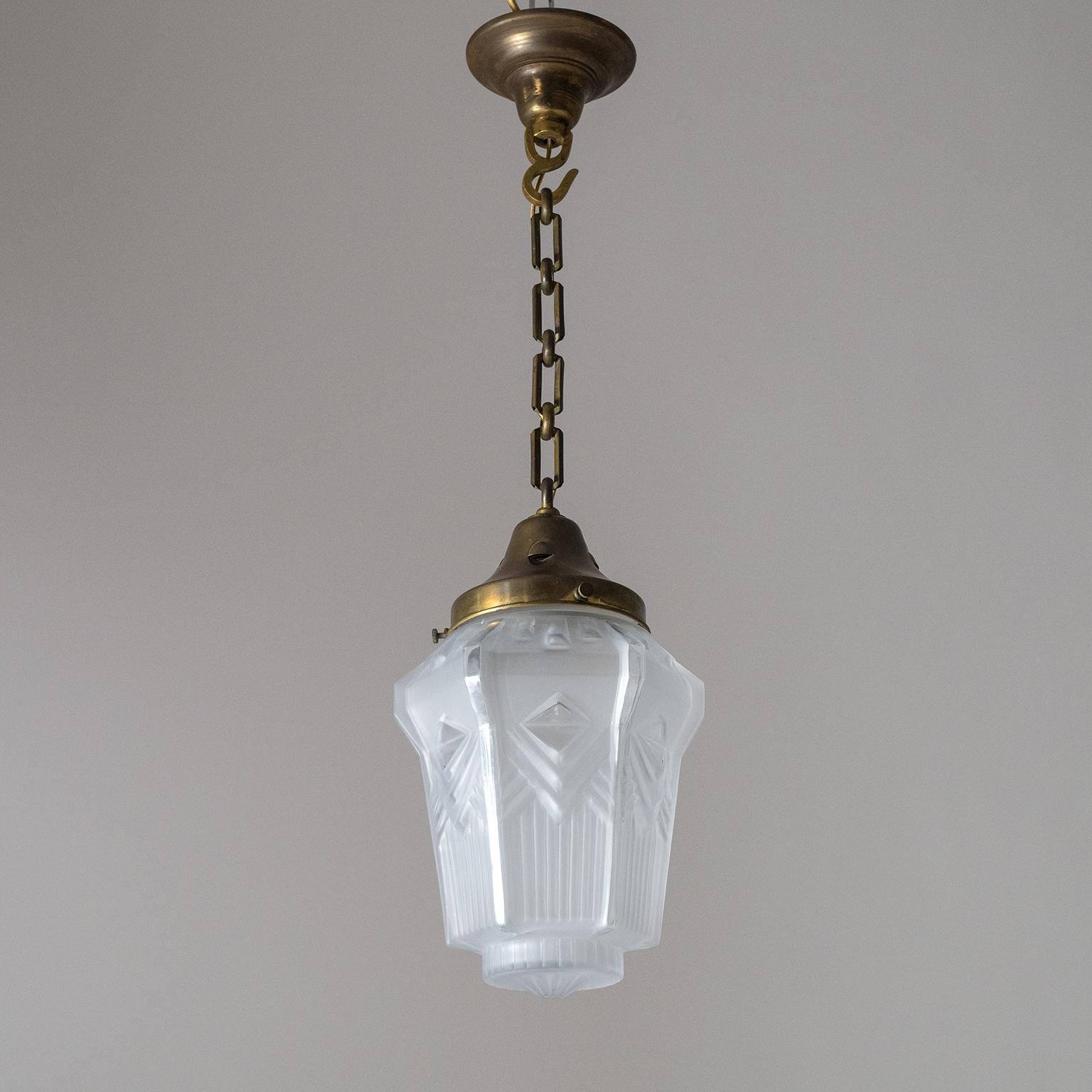 Fine French Art Deco glass and brass pendant from the 1920s. The hexagonal glass diffuser with intricate geometric and streamline patterns and texture is frosted on the outside with clear polished accents. The hardware is entirely in brass. One old