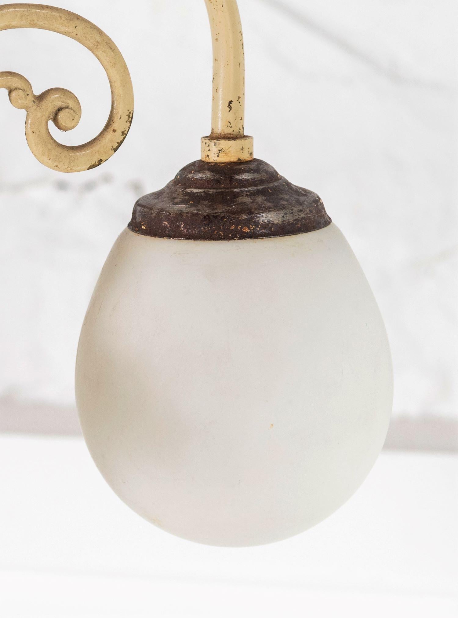 A stylish 1920s three arm chandelier with small opaline lamp shades. Three scroll arms made from solid brass on a central steel column, steel galleries with opaline droplet lamp shades.
Finished in its original enamel type cream paint which gives