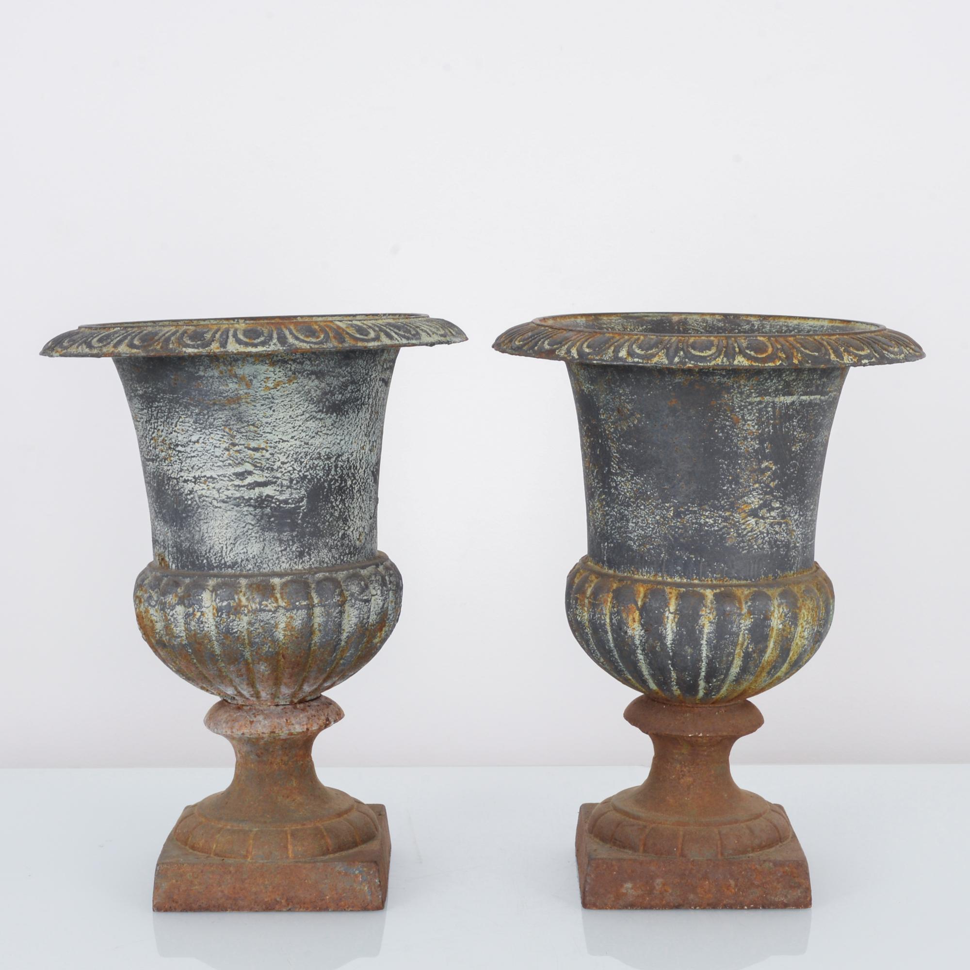 A pair of cast iron planters from France, circa 1920. An upturned bell-shape with a fluted cupola and broad lip, reminiscent of an inverted blossom elevated upon a stem. The tone of the metal has acquired a striking color gradient: steel blue and