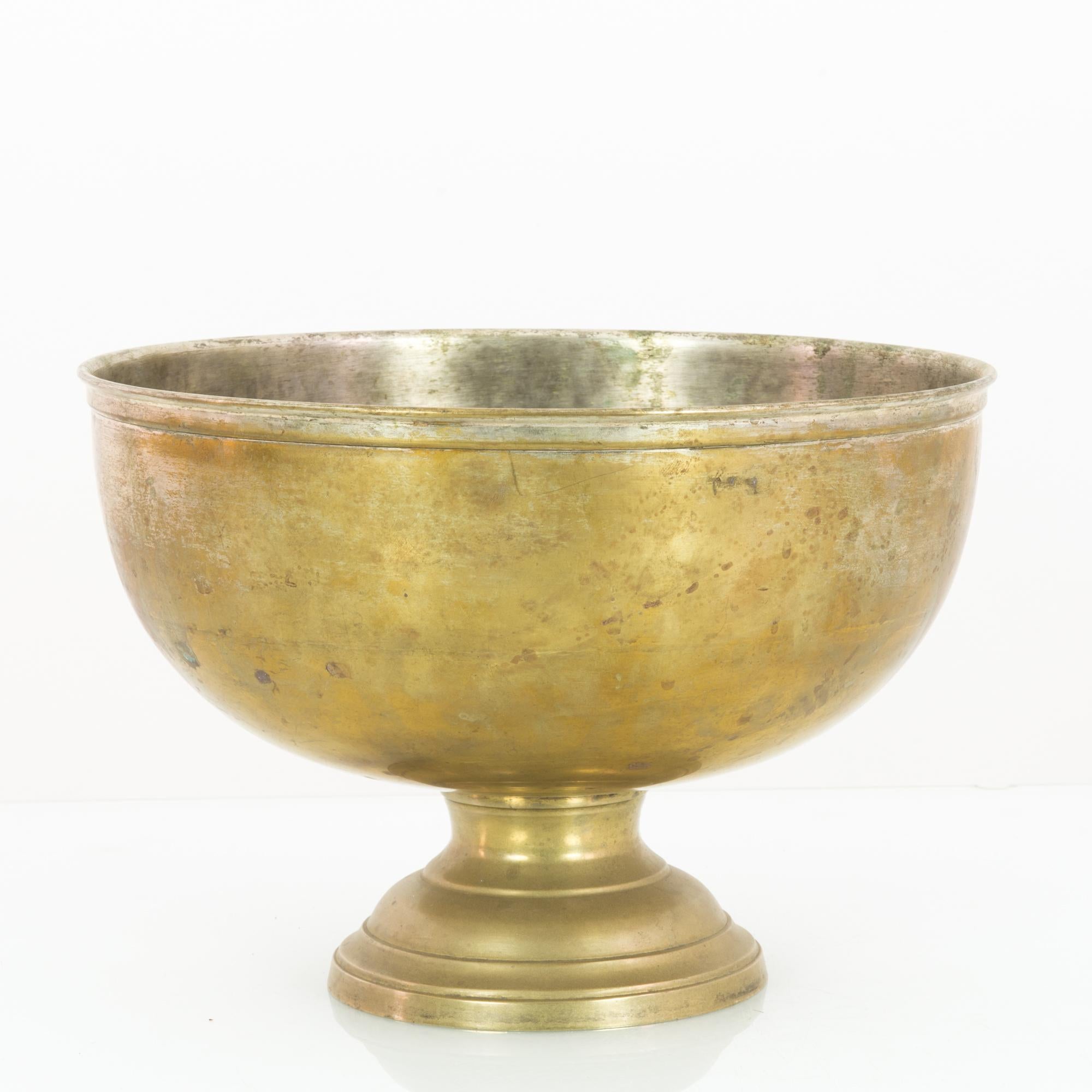 A brass bowl from France, circa 1920. A broad cup shape elevated on a low pedestal. The exterior surface has a muted gilded finish; the inside has worn to a silver shine. The patinated finish, smoothed and tarnished, adds to the impression of an