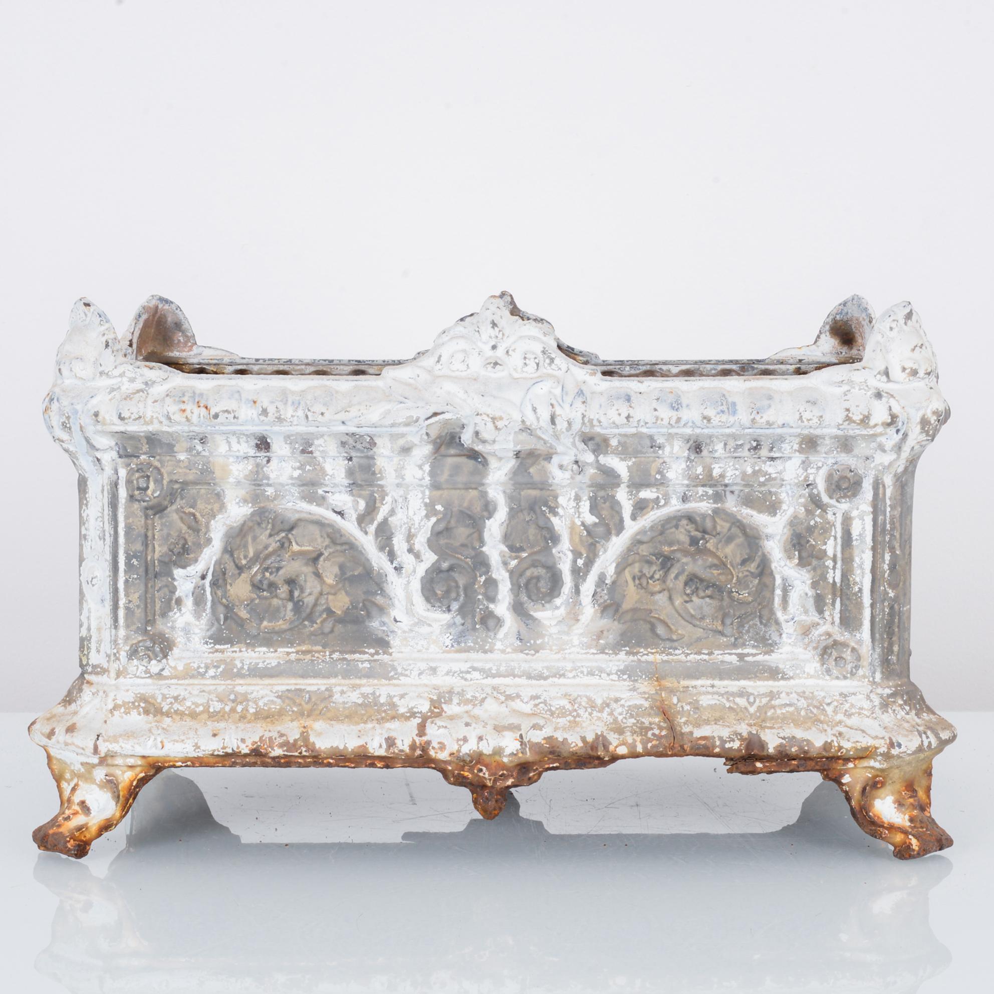 This cast iron planter was made in France, circa 1920. Raised on scroll feet, the planter features elaborate molding and floral motifs, making it a charming Rococo Revival piece. The distressed white paint complements the sheen of the cast iron in