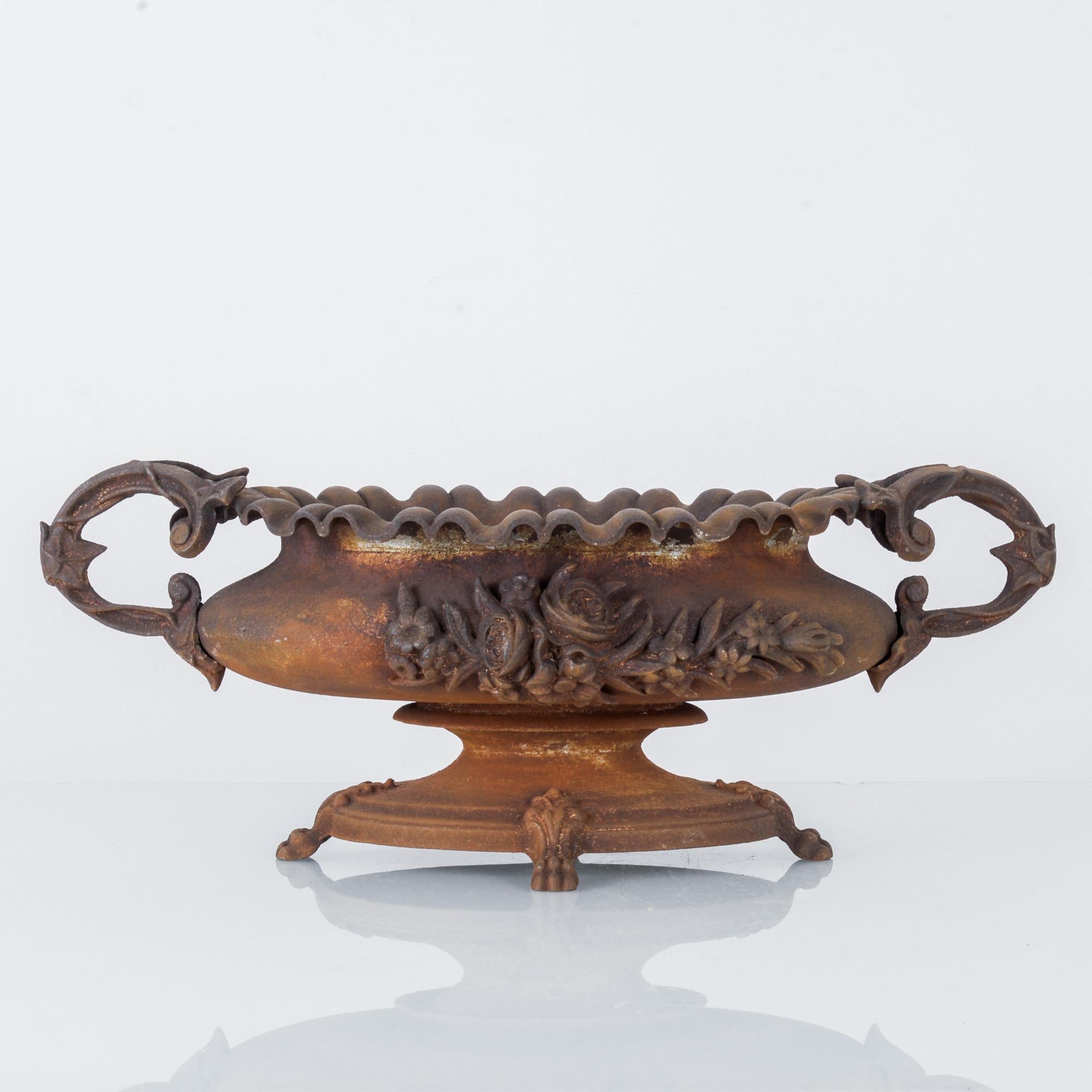 This cast iron planter was made in France, circa 1920. In the Rococo Revival style, the planter displays expressive curves and elaborate ornamentation of flowers and leaves. It features a scalloped top and stands on a circular base raised by claw